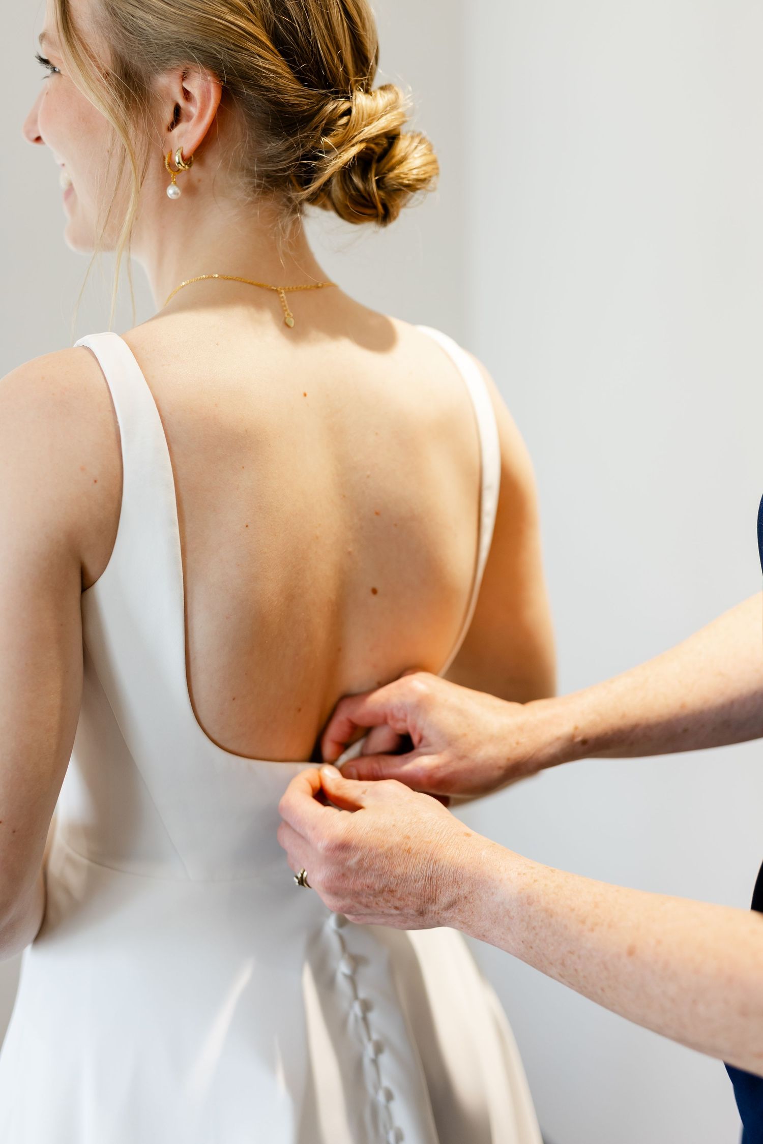 Close-up of hands adjusting the back buttons of a classic white wedding gown.