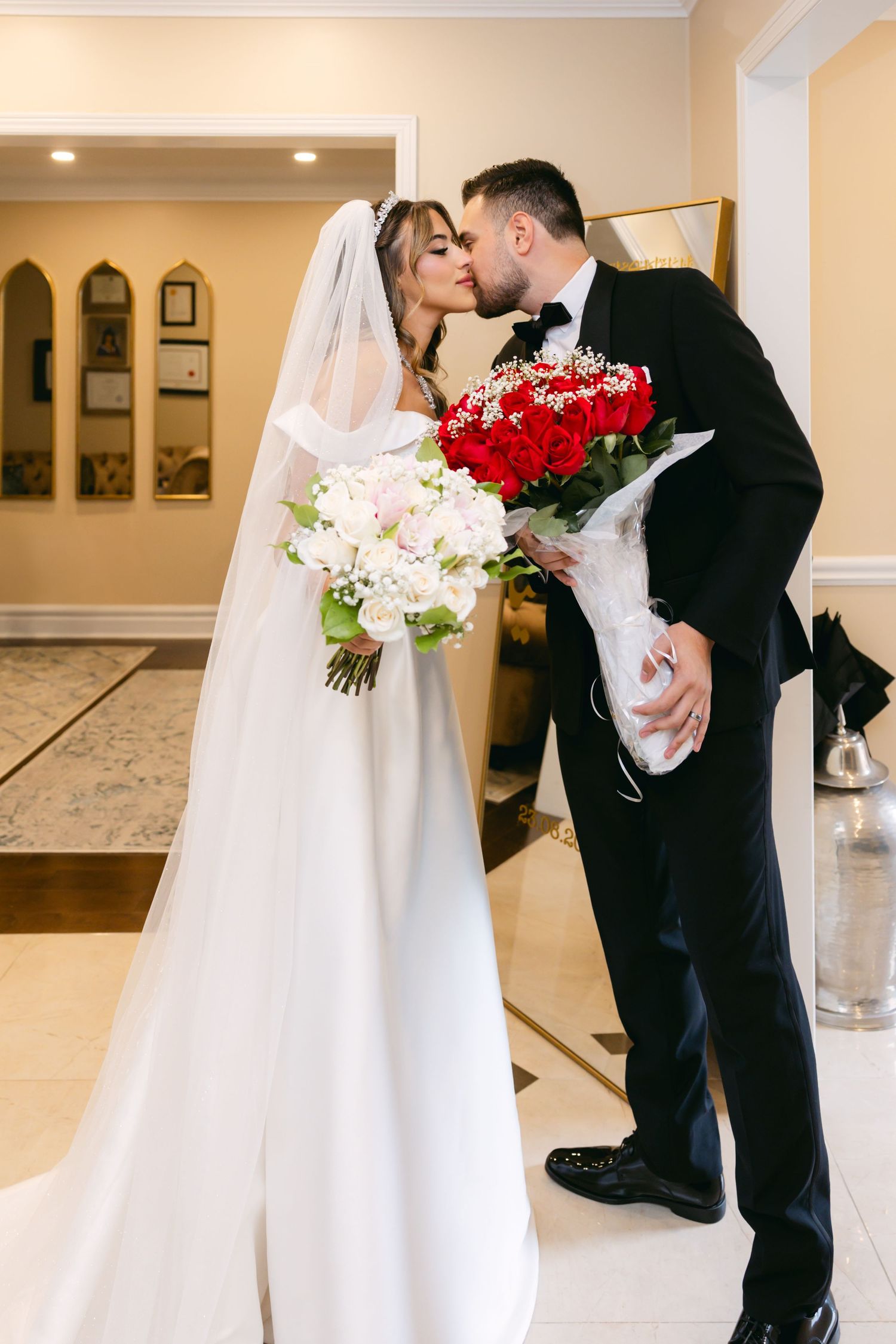 Wedding couple embracing in elegant indoor venue with cream colored walls.