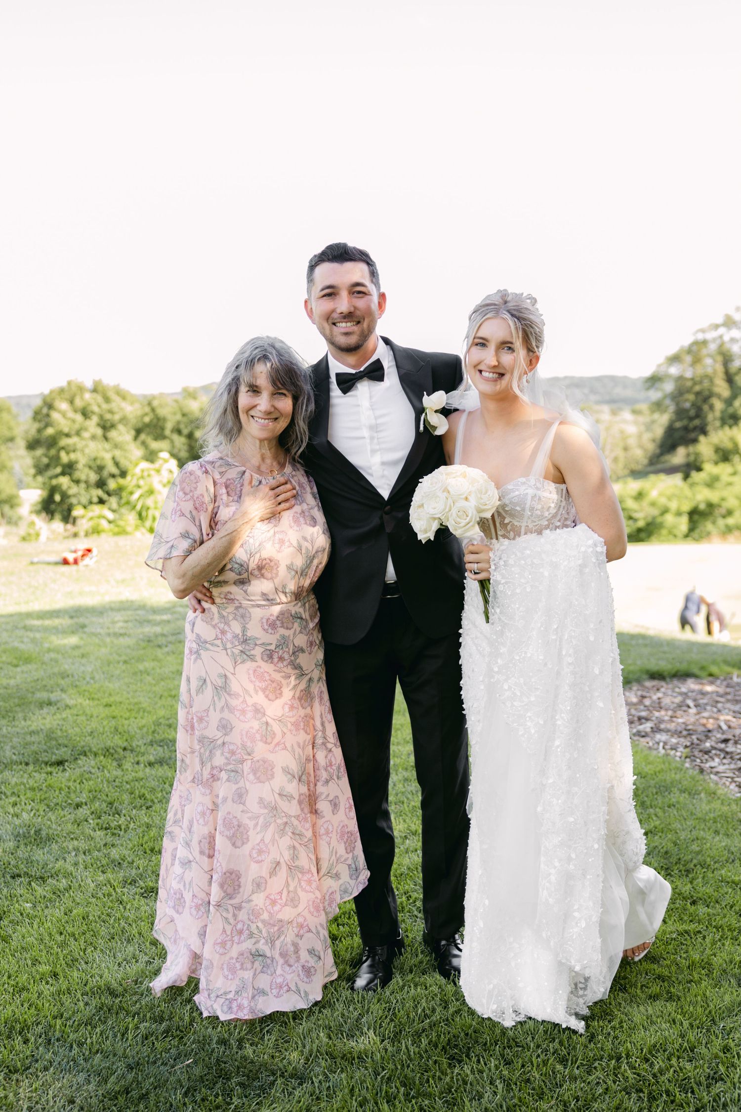Wedding party posing on grass with bride wearing detailed white lace gown.