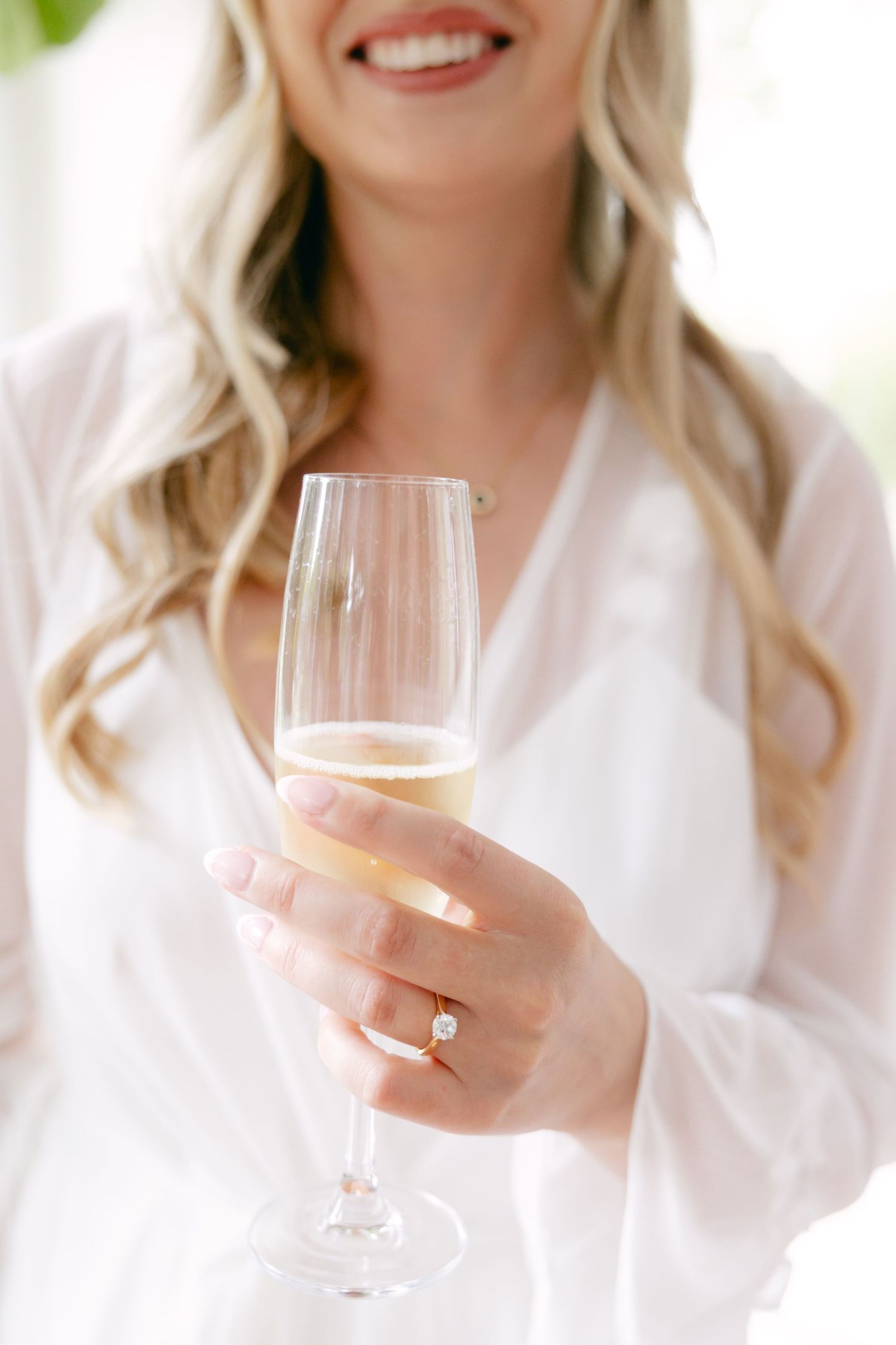 Women in white robes hold champagne glasses while smiling and celebrating.
