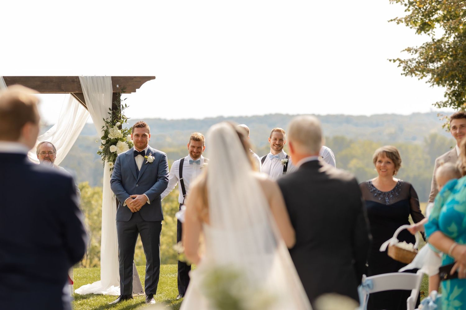 Wedding ceremony in progress with guests seated on lawn under sunny skies.