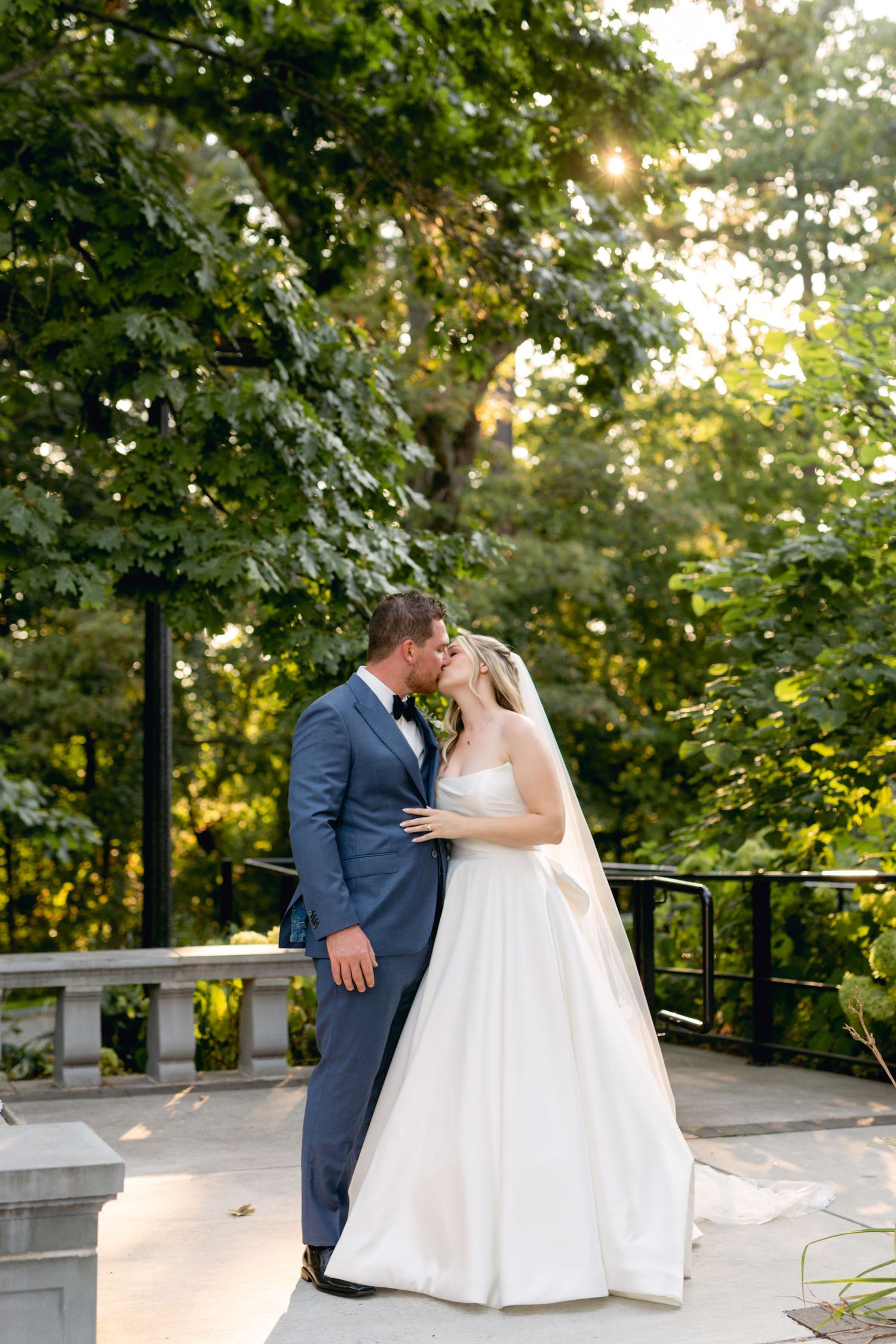 Wedding couple shares romantic moment on stone balcony surrounded by trees.