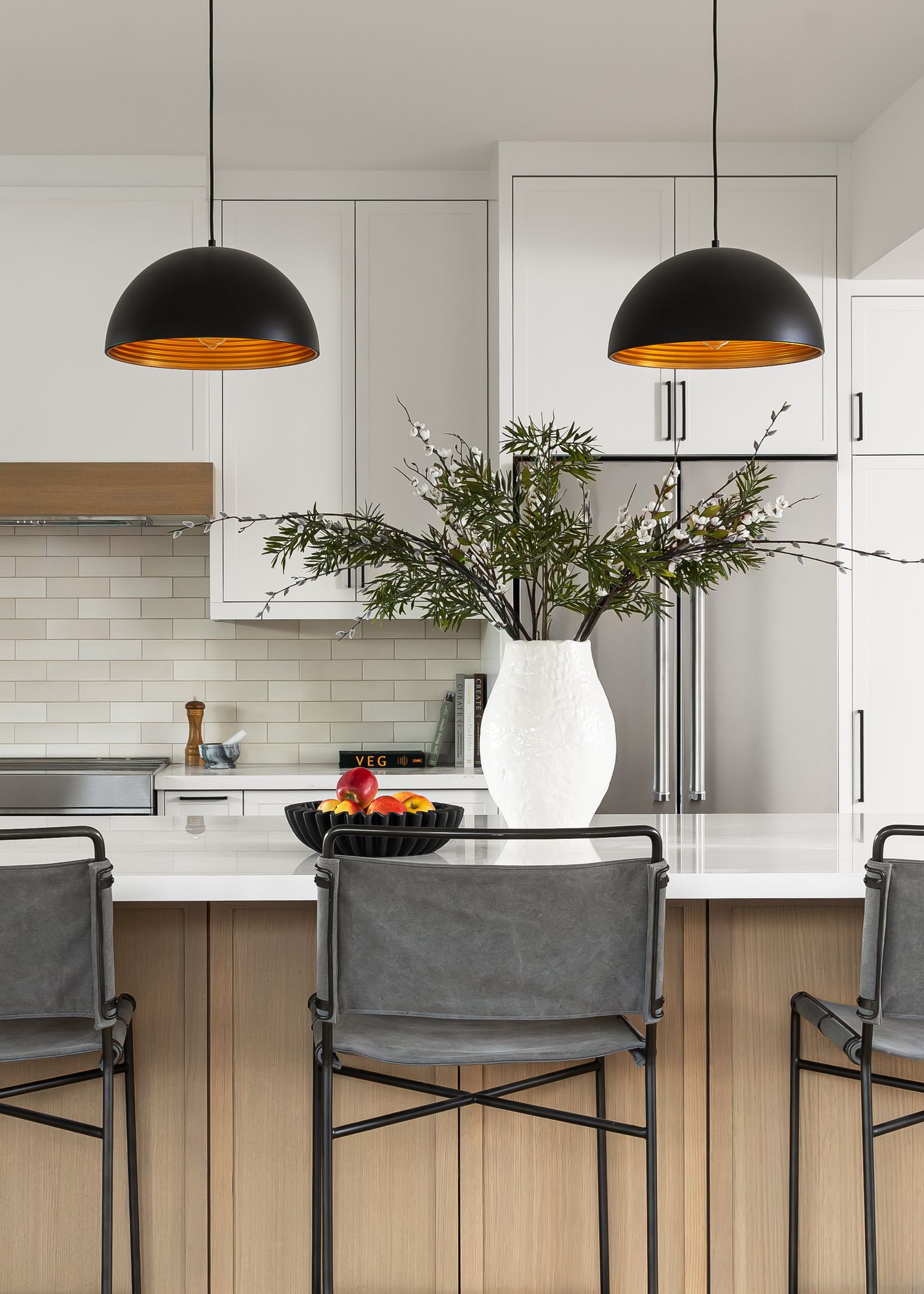 Modern kitchen with black pendant lights, grey bar stools, and white subway tile backsplash.