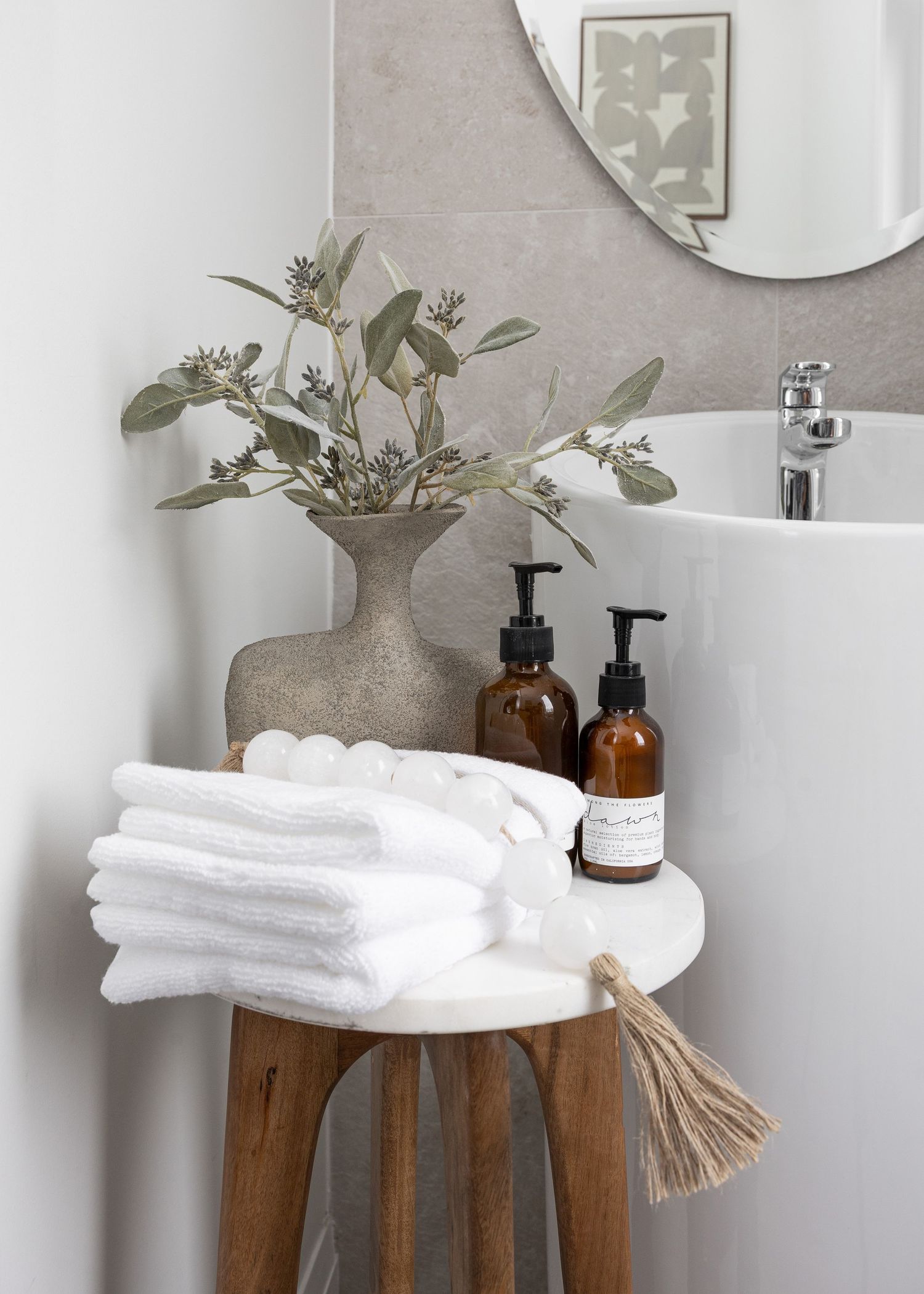 Spa-like bathroom counter with wooden stand, white towels and glass dispensers.