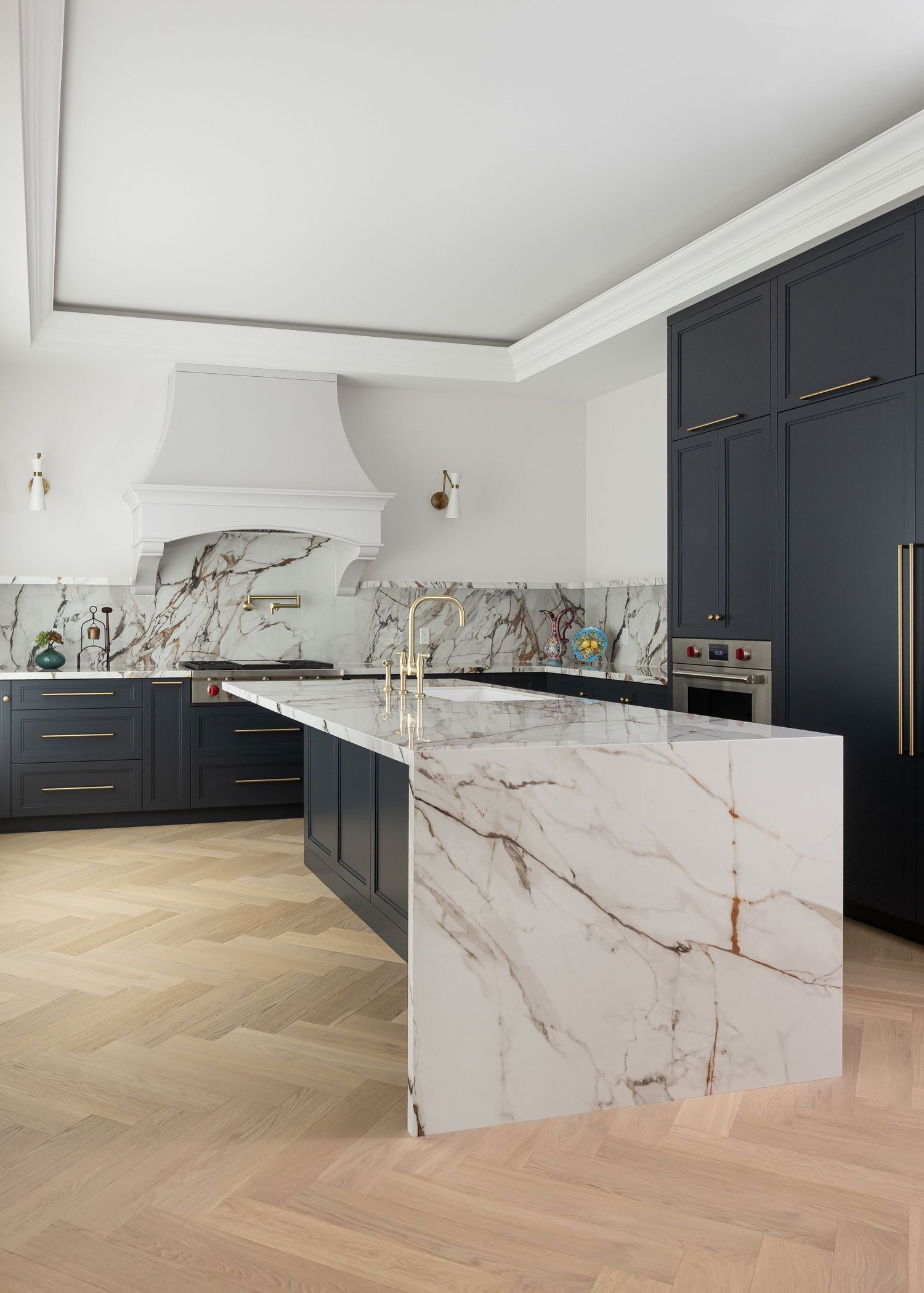 Luxurious kitchen featuring marble waterfall island, dark cabinets, and light hardwood flooring.