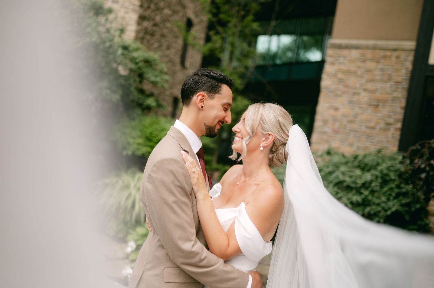 First look moment captured between couple in elegant wedding attire against stone wall backdrop.