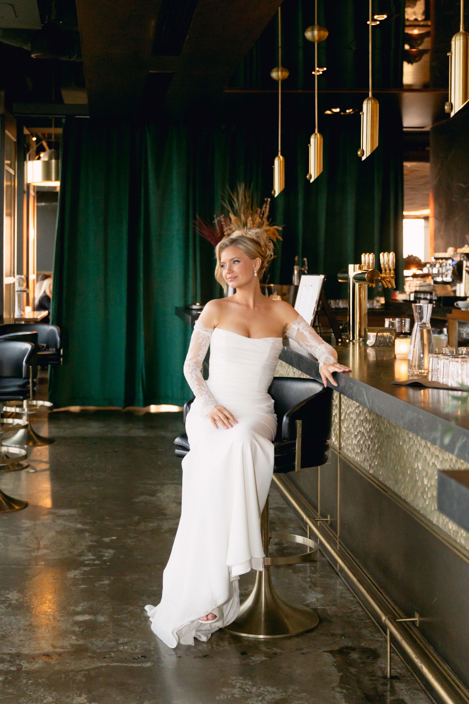Beautiful bride wearing a white strapless gown with lace sleeves posing at a moody upscale bar.