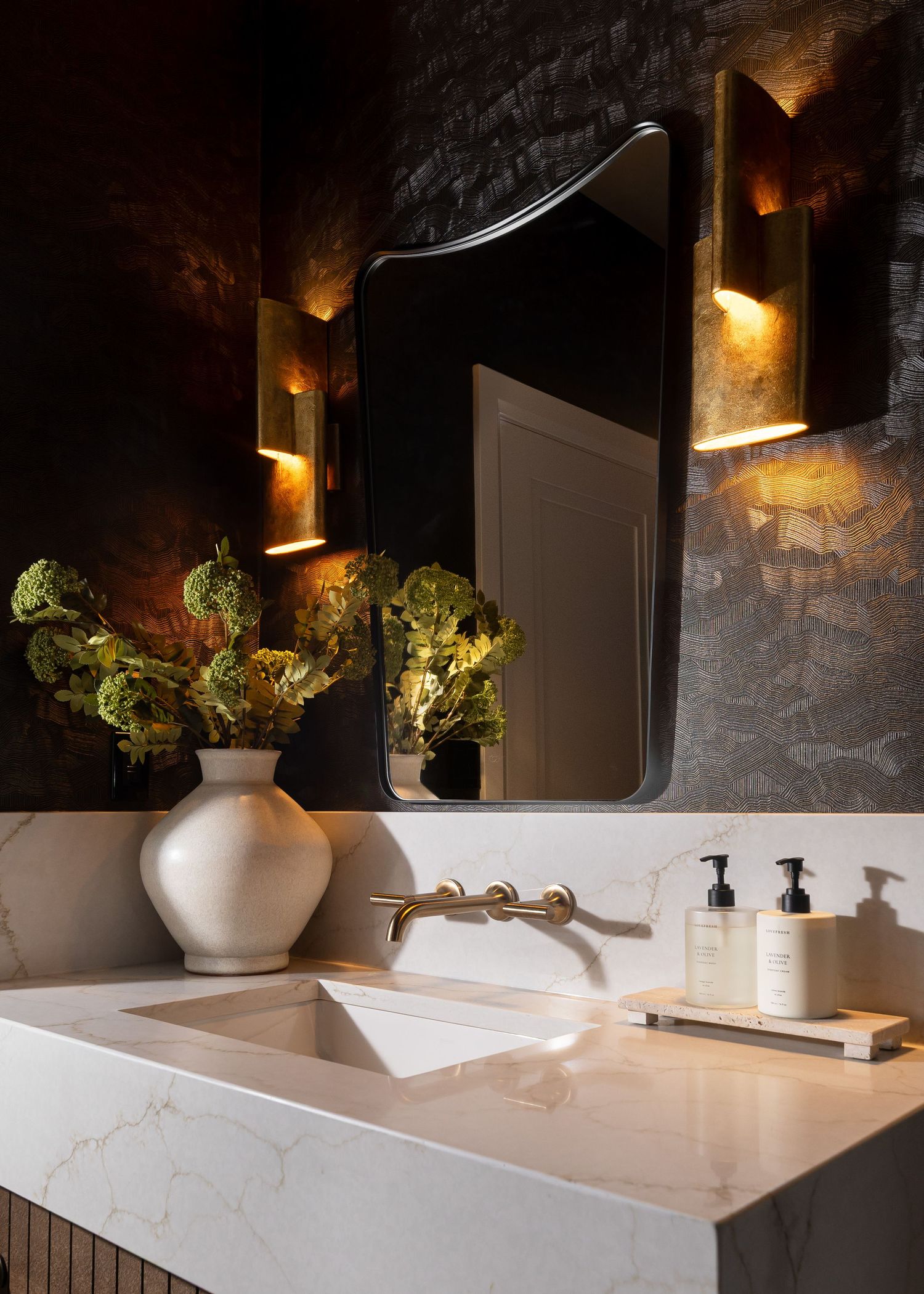 Modern bathroom featuring white marble countertops, dark textured walls, and elegant sconce lighting.