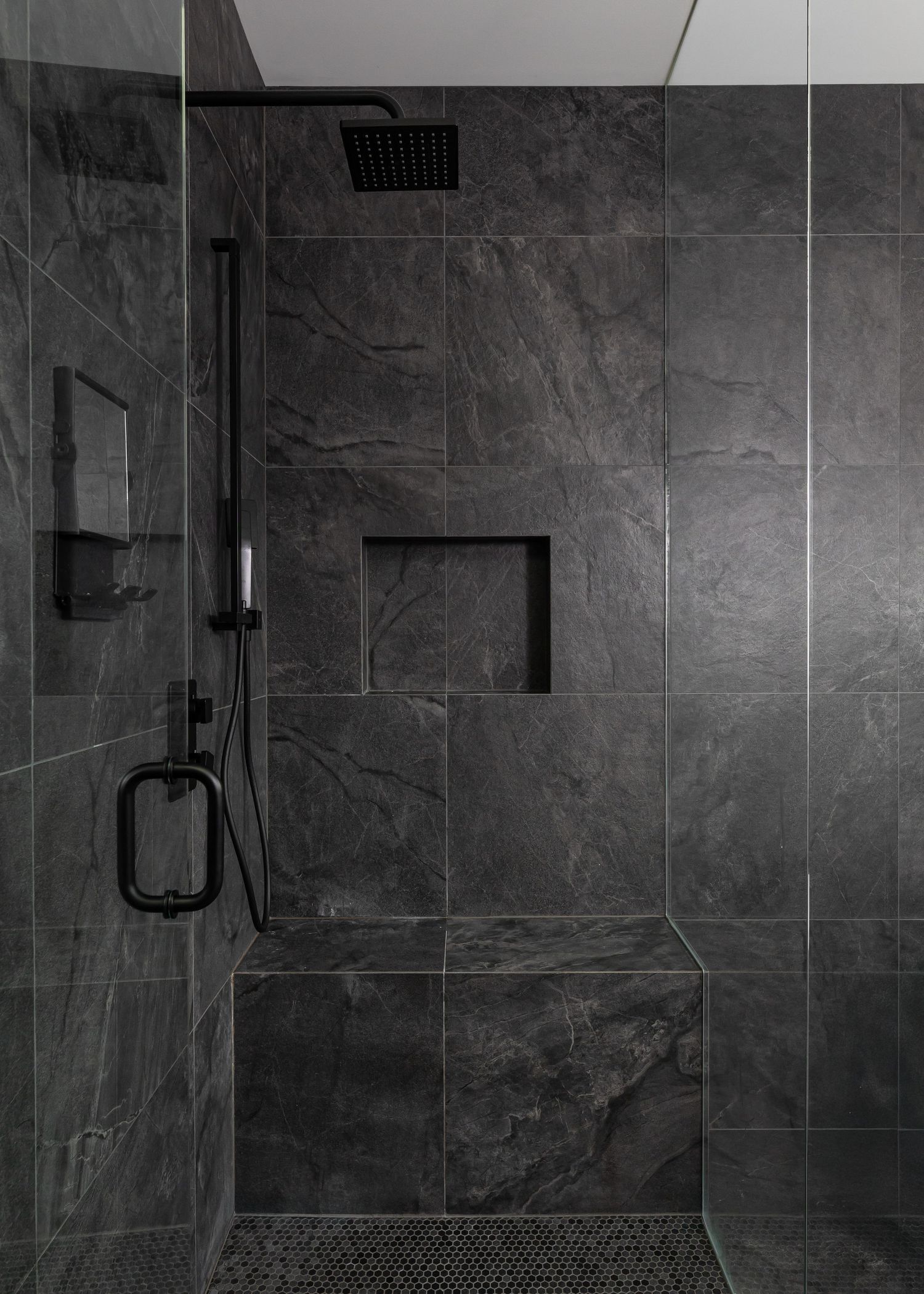 Modern shower enclosure with dark gray marble tile walls and black fixtures.