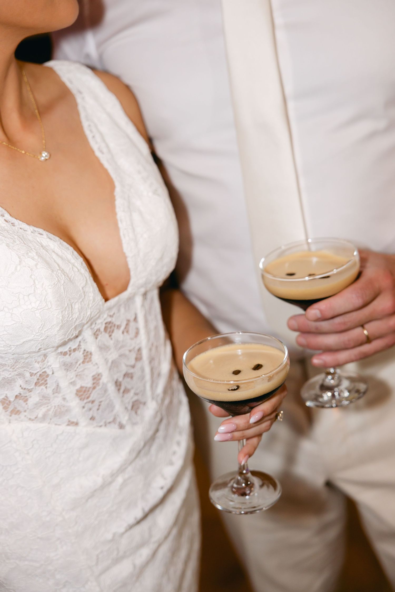 Close-up shot of a white lace wedding dress and cocktail glass being held at a reception.