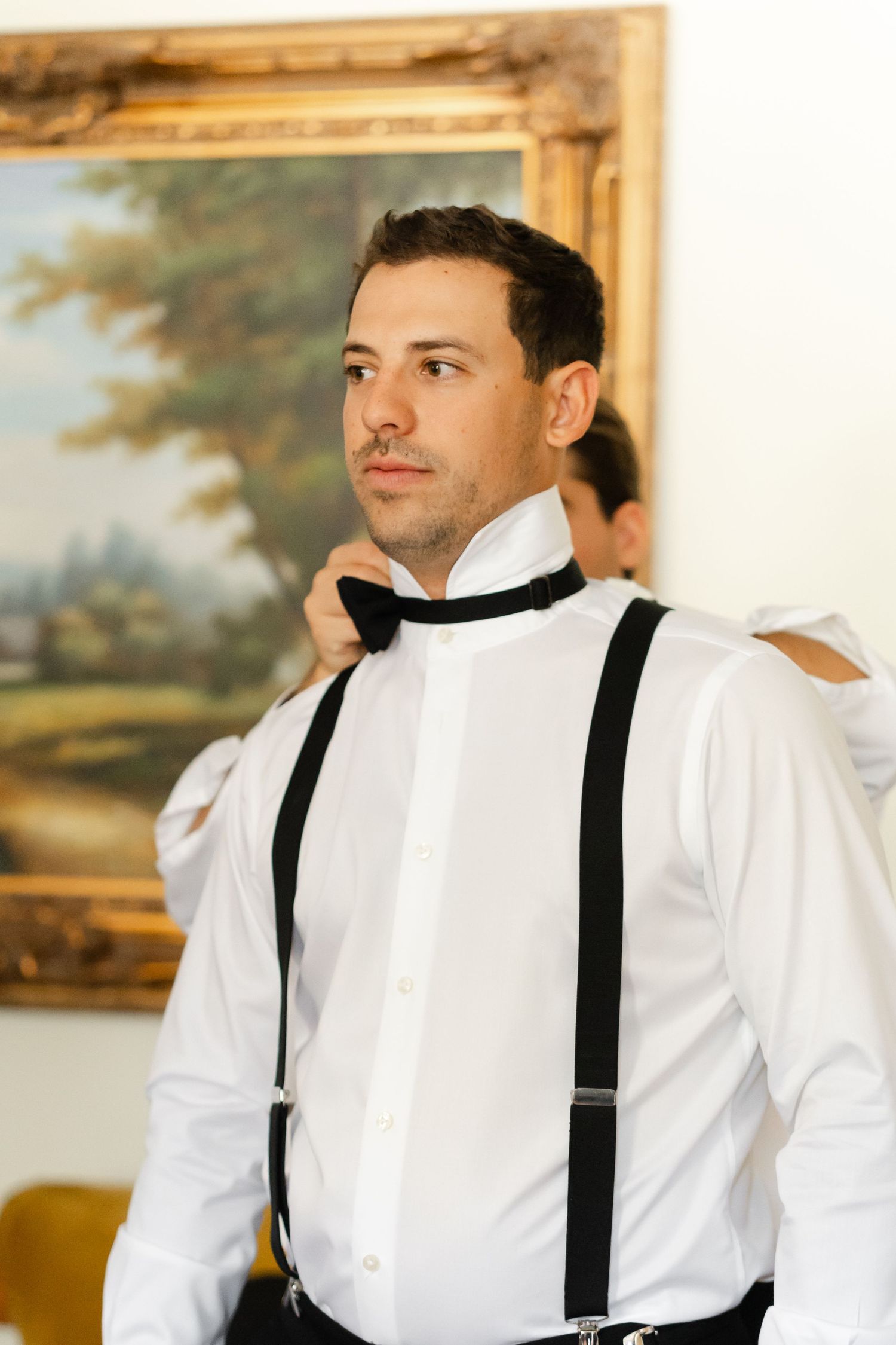 Groomsman adjusting black suspenders over crisp white dress shirt.