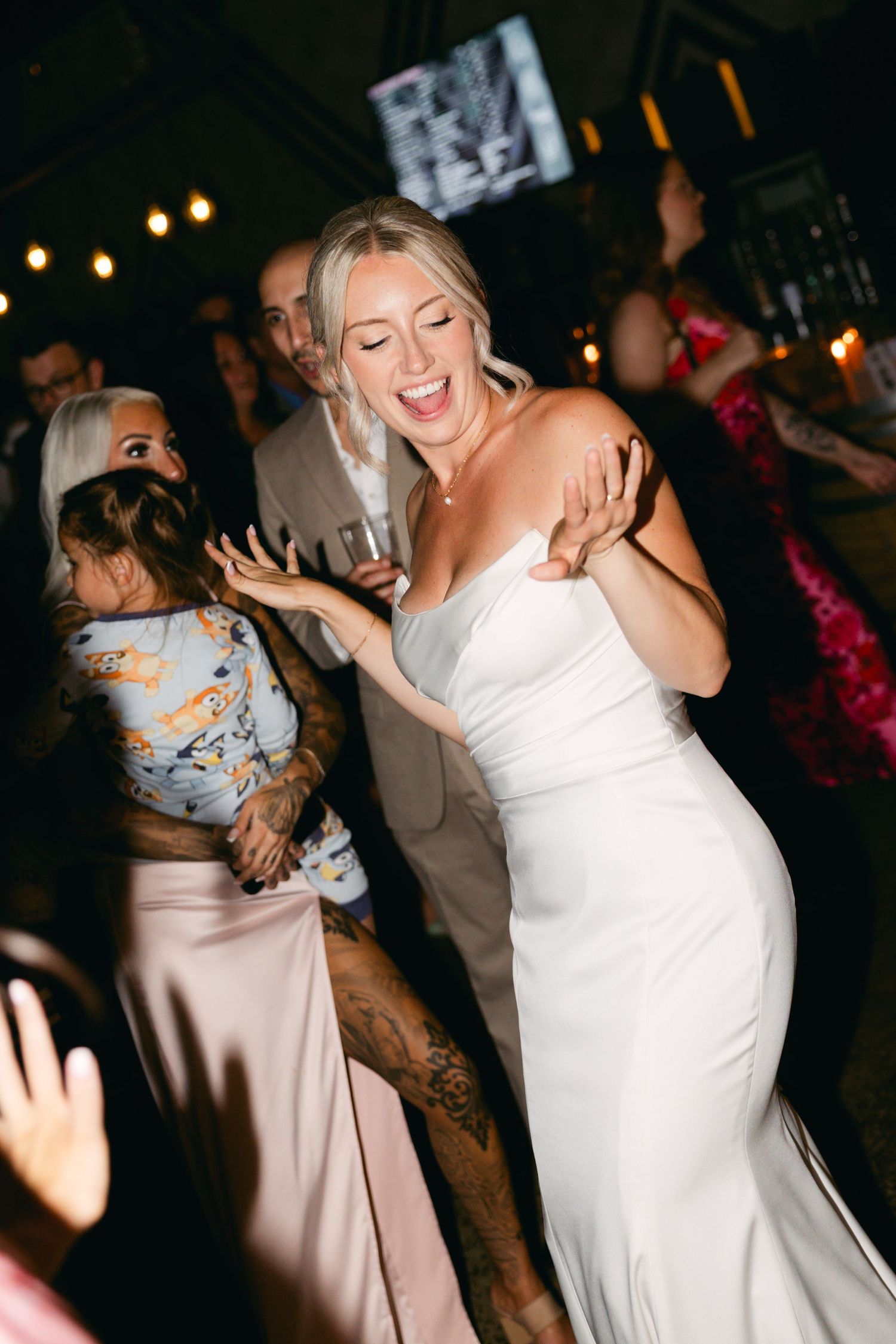 Wedding guests dancing and celebrating on a dimly lit dance floor with string lights overhead.