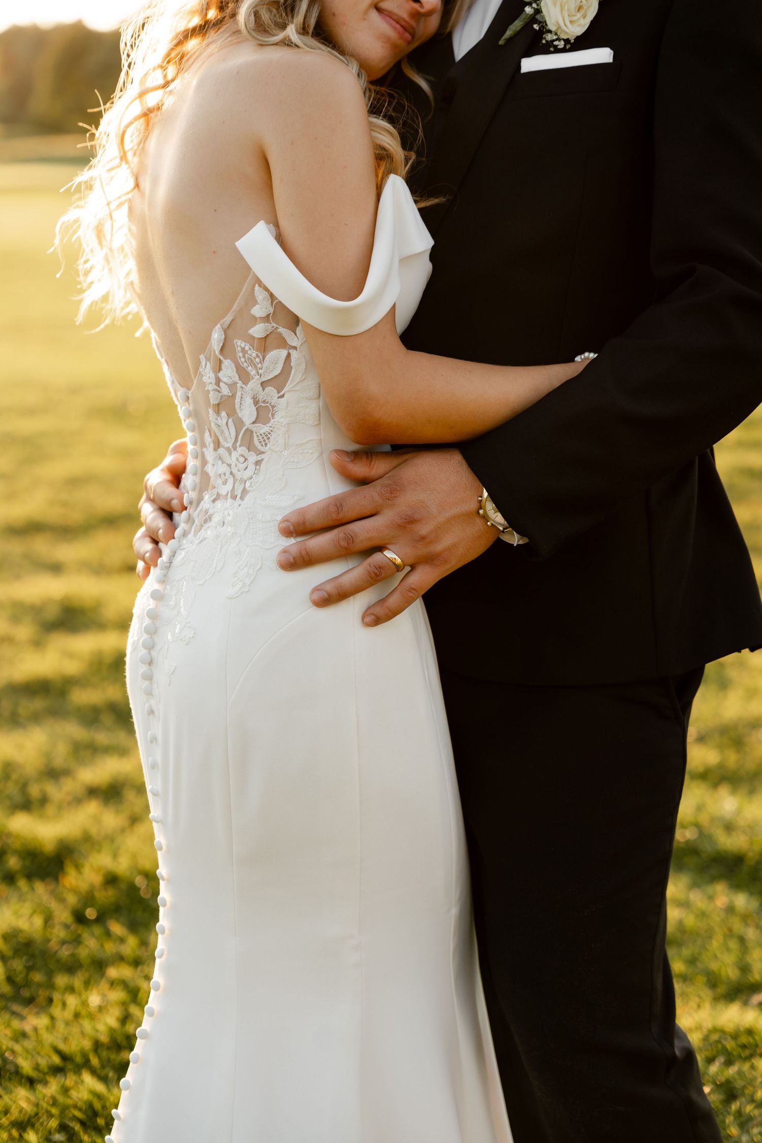 Close-up detail of a white lace wedding dress and embrace during golden hour.