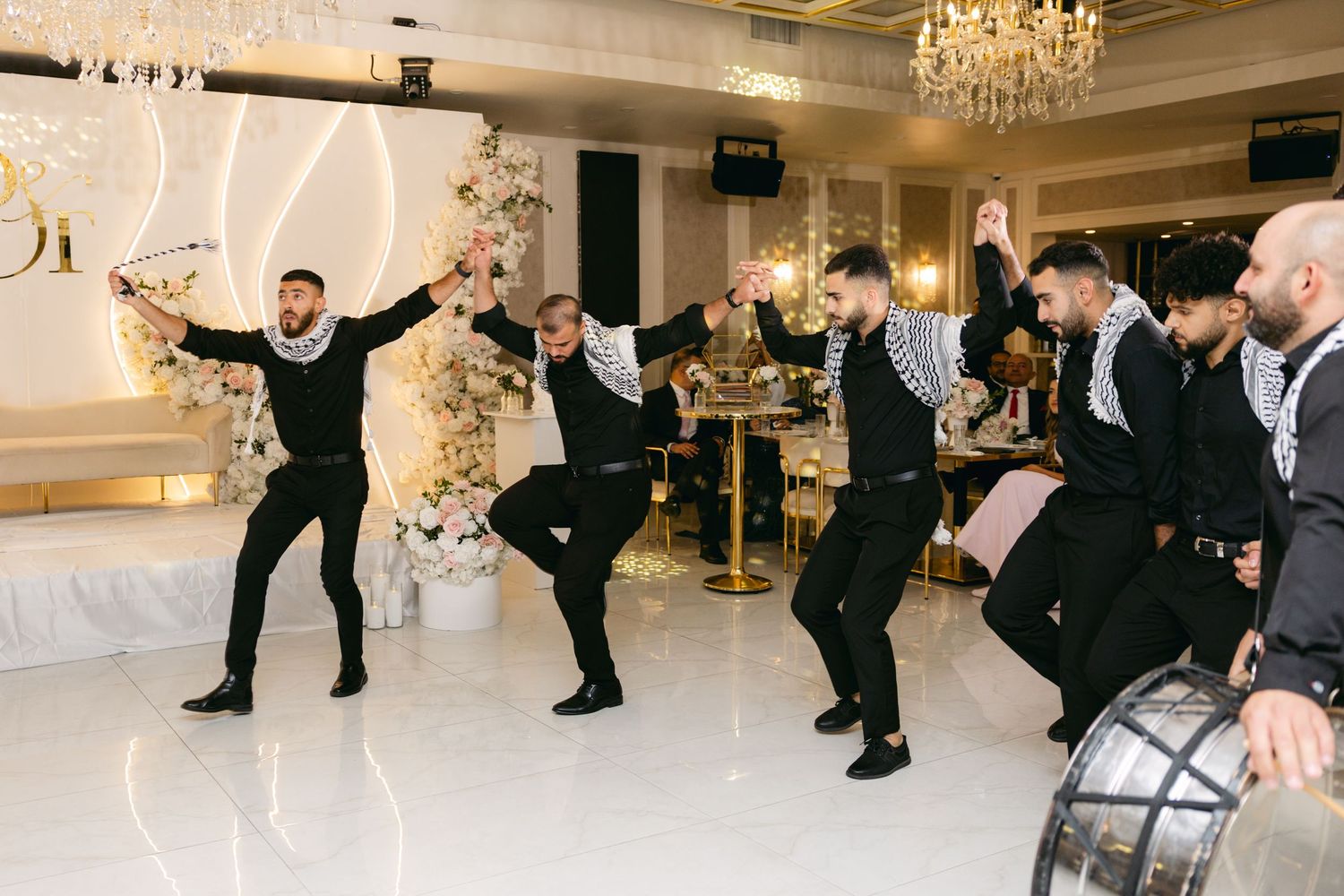 Wedding guests performing traditional dance moves in a luxurious ballroom setting.