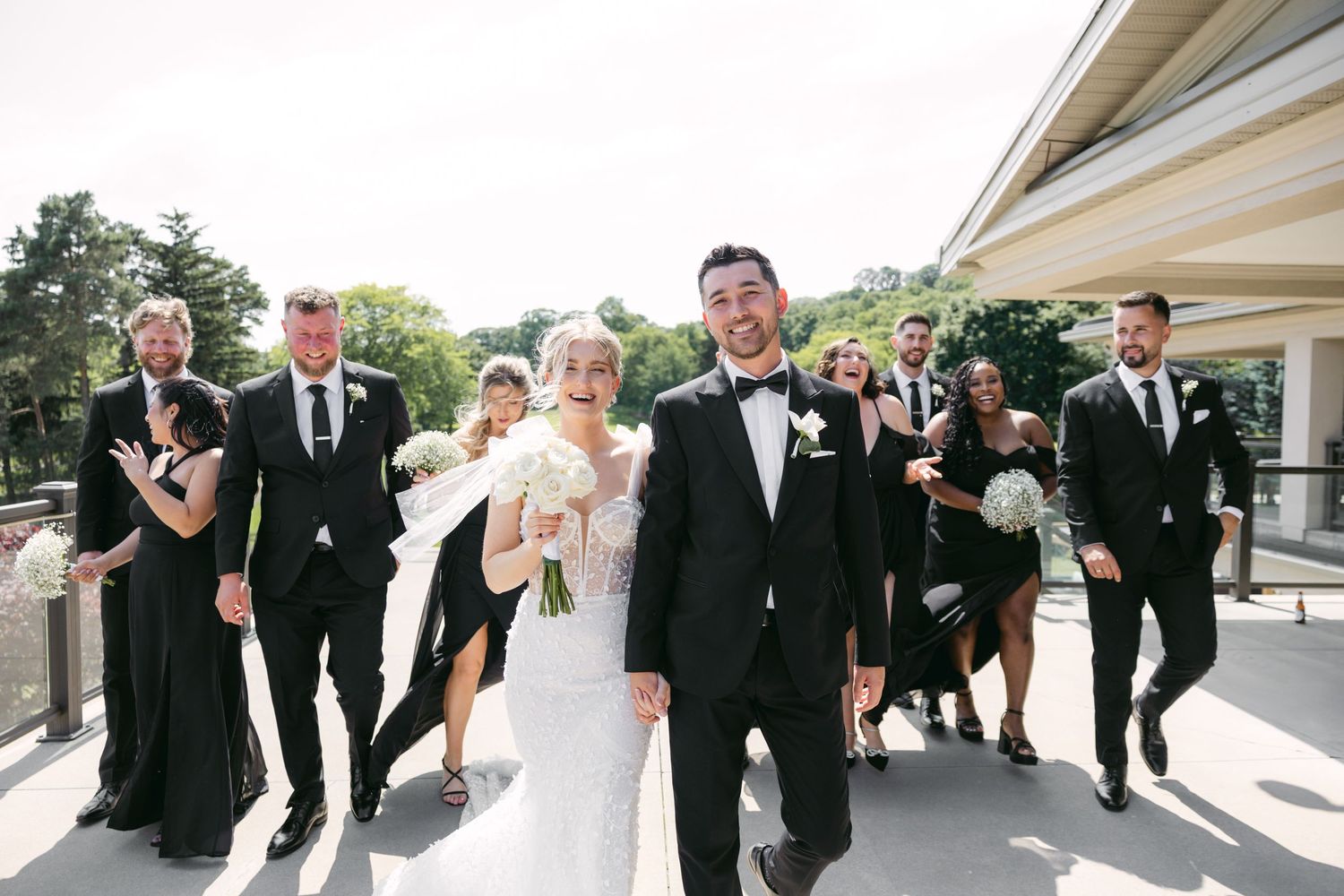 Wedding party members celebrate joyfully on outdoor venue patio in formal attire.