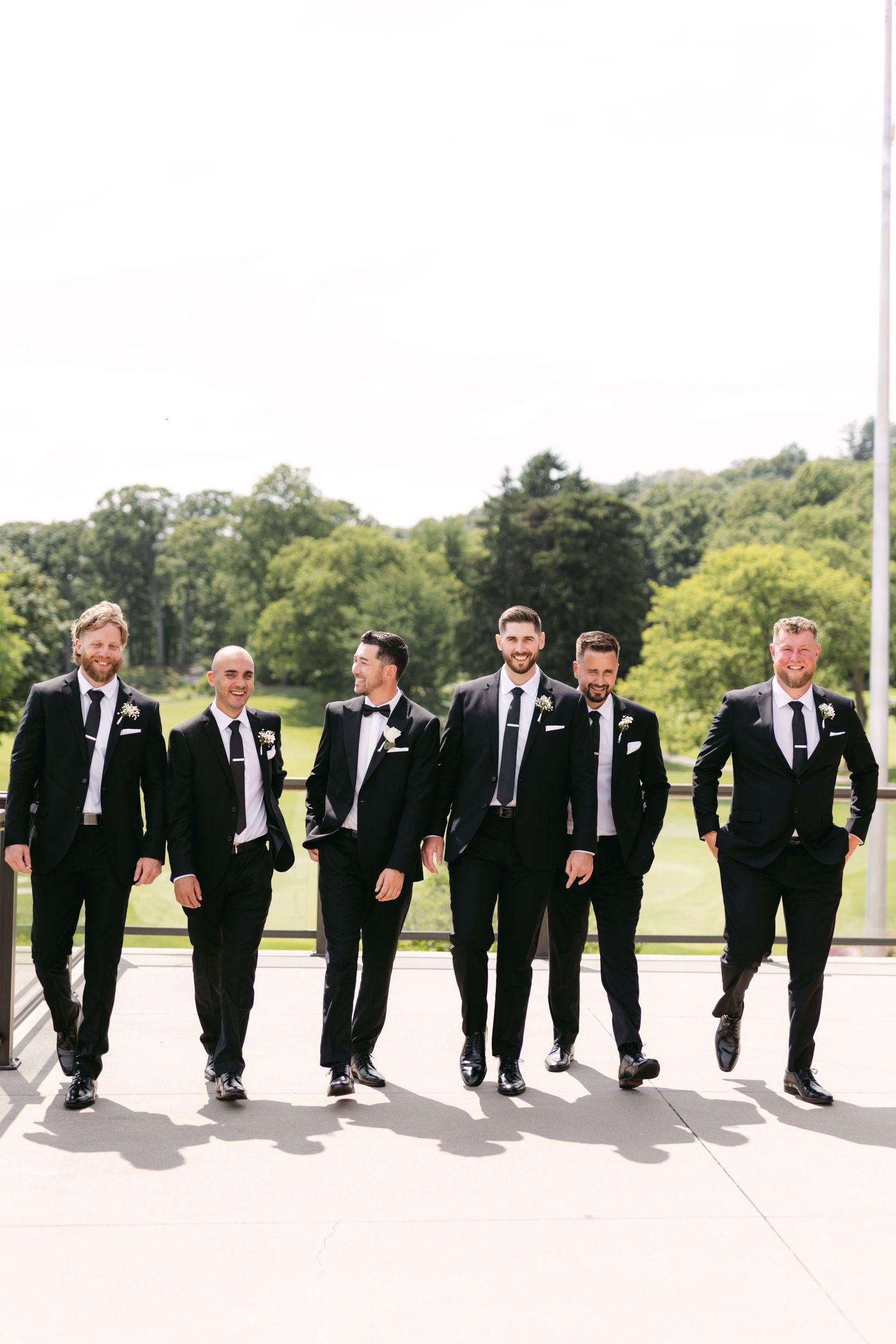 Wedding party of groomsmen walking in black suits on a sunny day.
