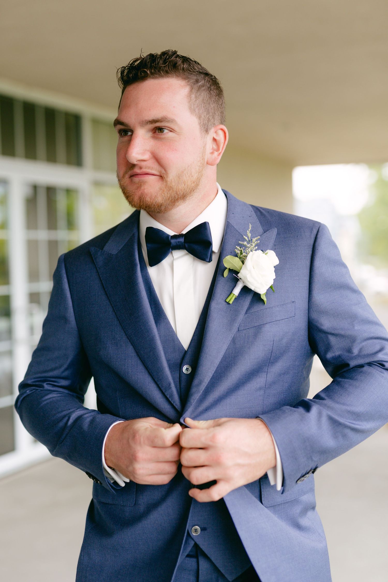 Person adjusting navy blue wedding suit with bow tie and white boutonniere.
