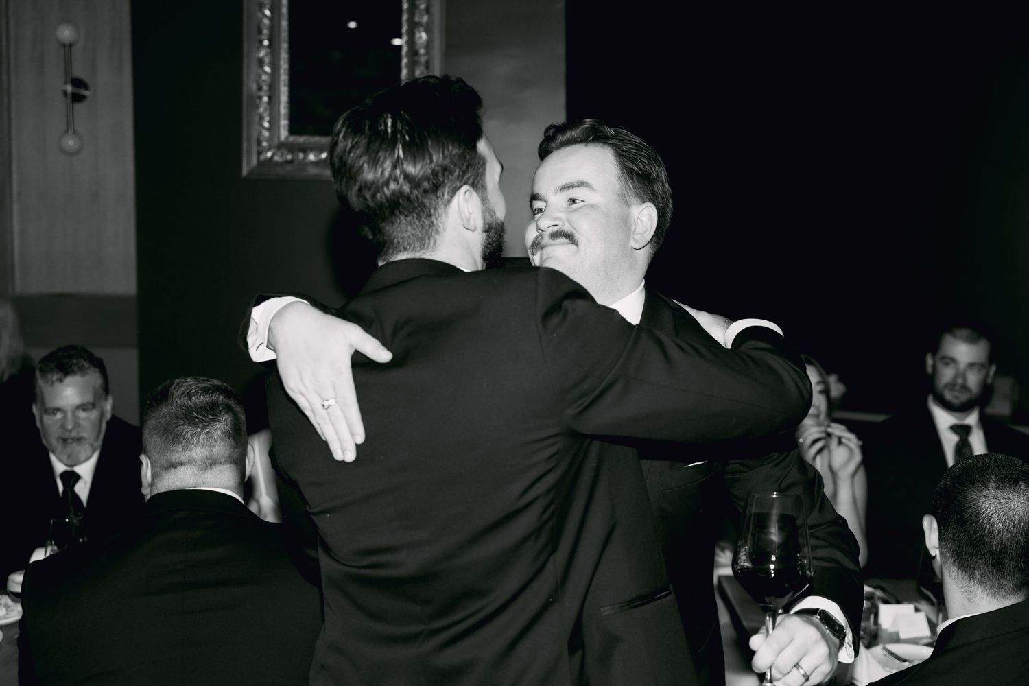Groom sharing warm embrace with guest during black and white wedding reception photo.