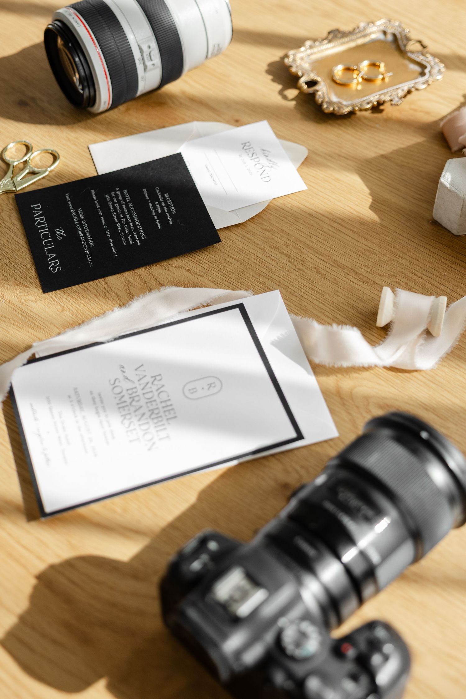 Photography equipment and business cards arranged on wooden desk with camera lens and ribbons.