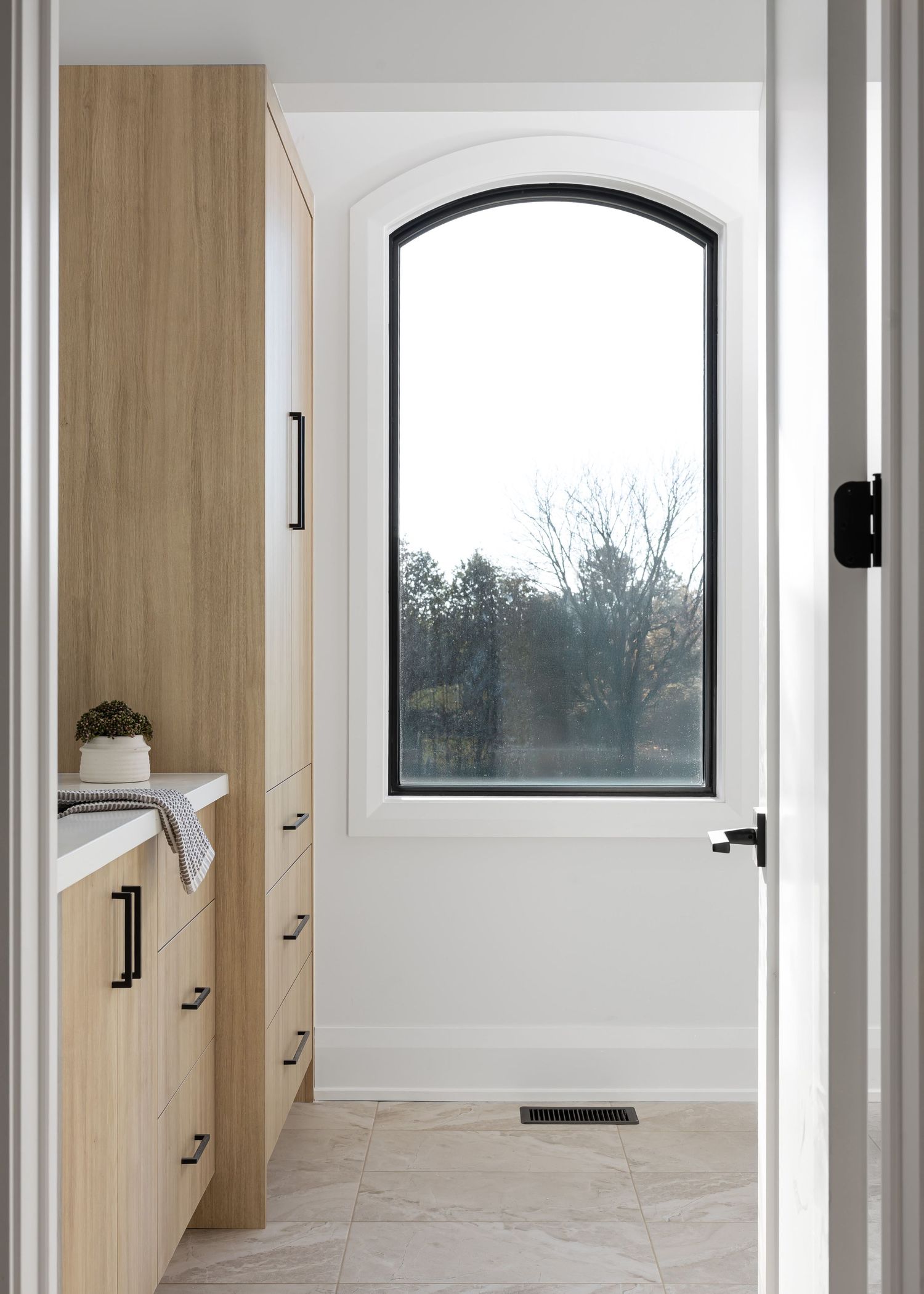 Walk-in closet features floor-to-ceiling wood cabinets and an arched window bringing in natural light.