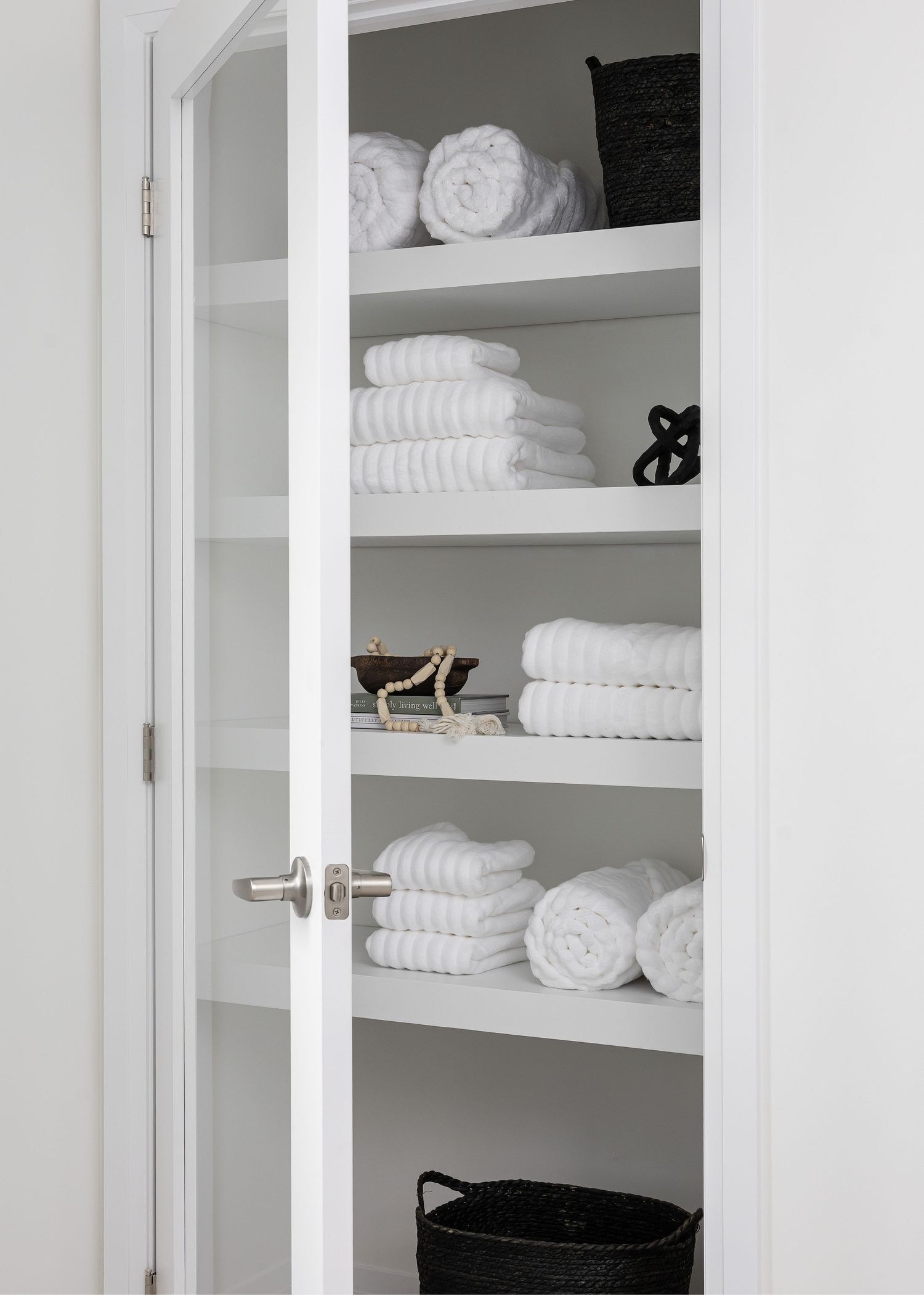 Organized linen closet with white towels neatly folded on multiple shelves.