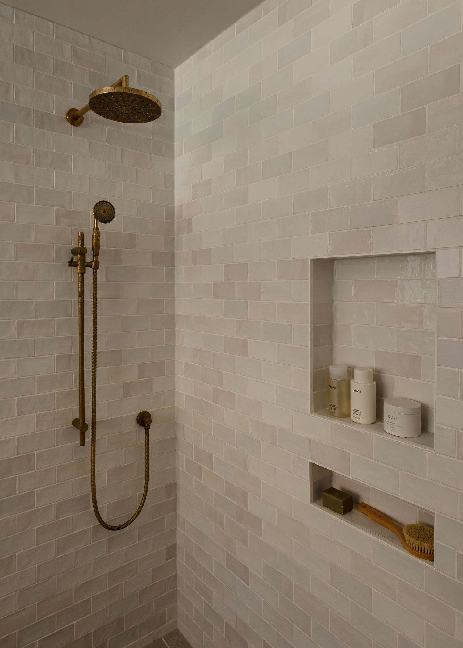 Elegant shower space with light brick tiles, brass fixtures, and built-in storage niches.