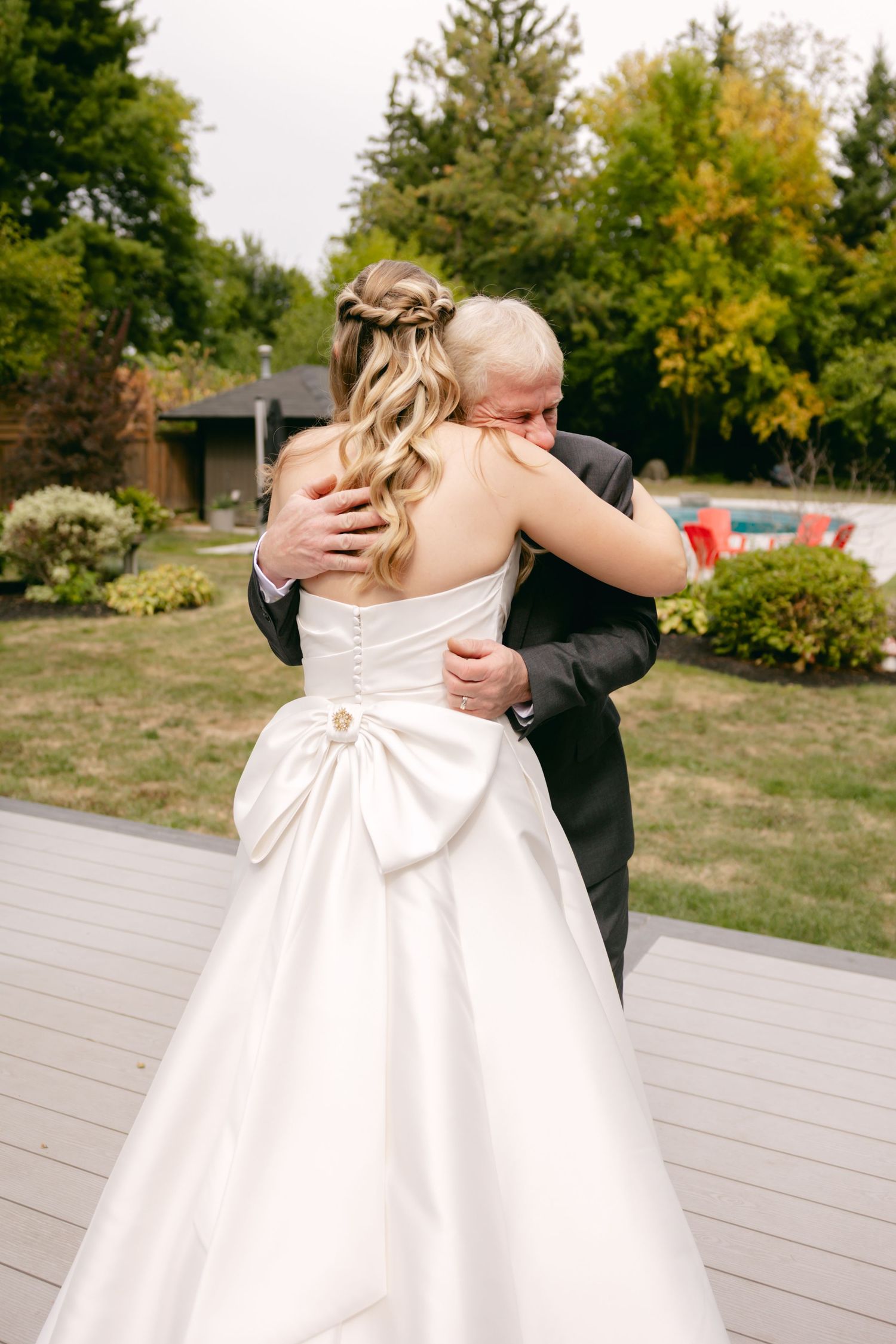 An emotional embrace between a bride in a white wedding gown and someone in a dark suit during an outdoor ceremony.