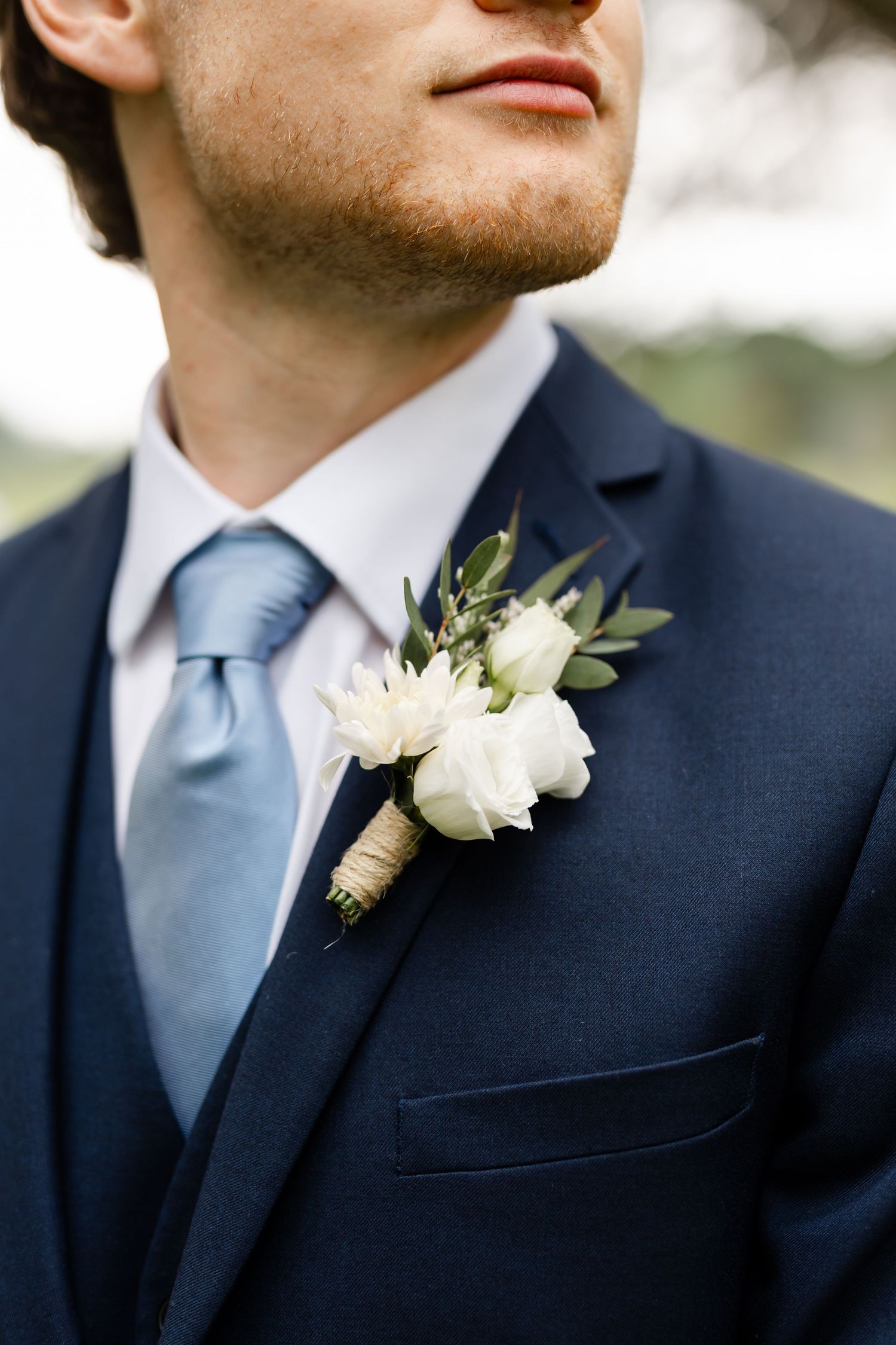 Close-up of a navy suit with light blue tie and white floral boutonniere at a wedding.