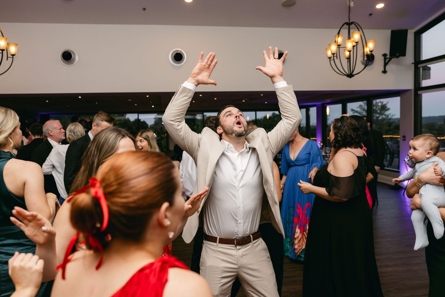 Wedding party dancing with raised hands and energetic movements during reception celebration.