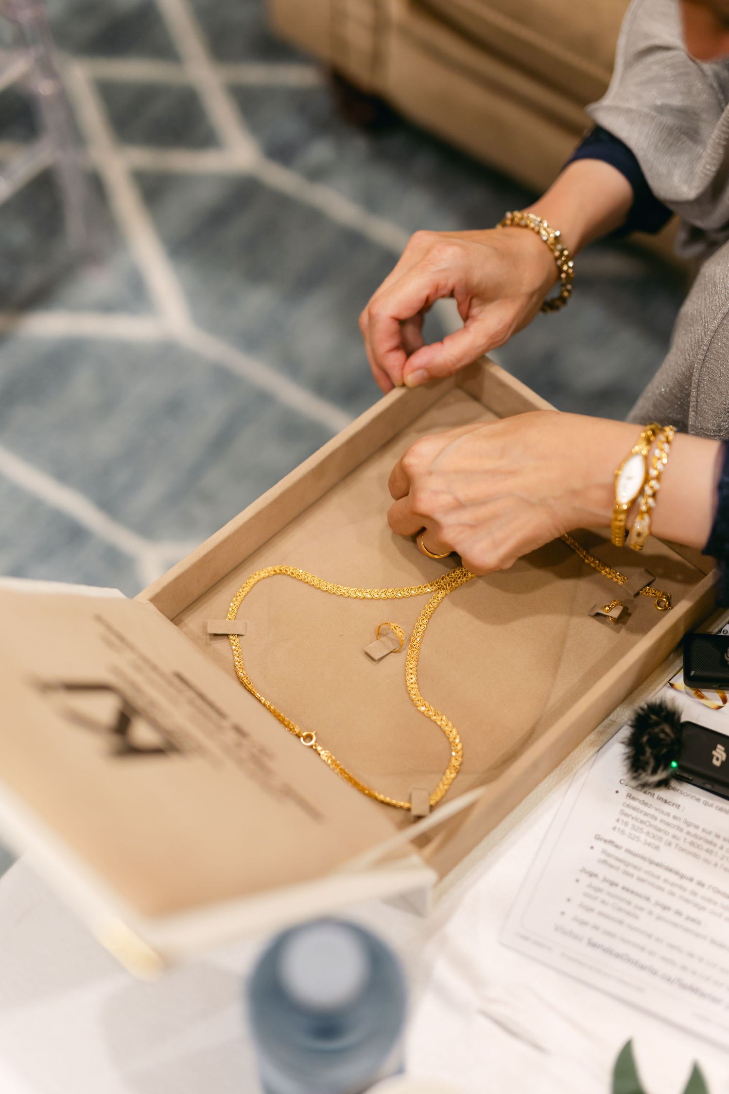 Hands arranging a gold chain necklace on a beige surface next to documents.
