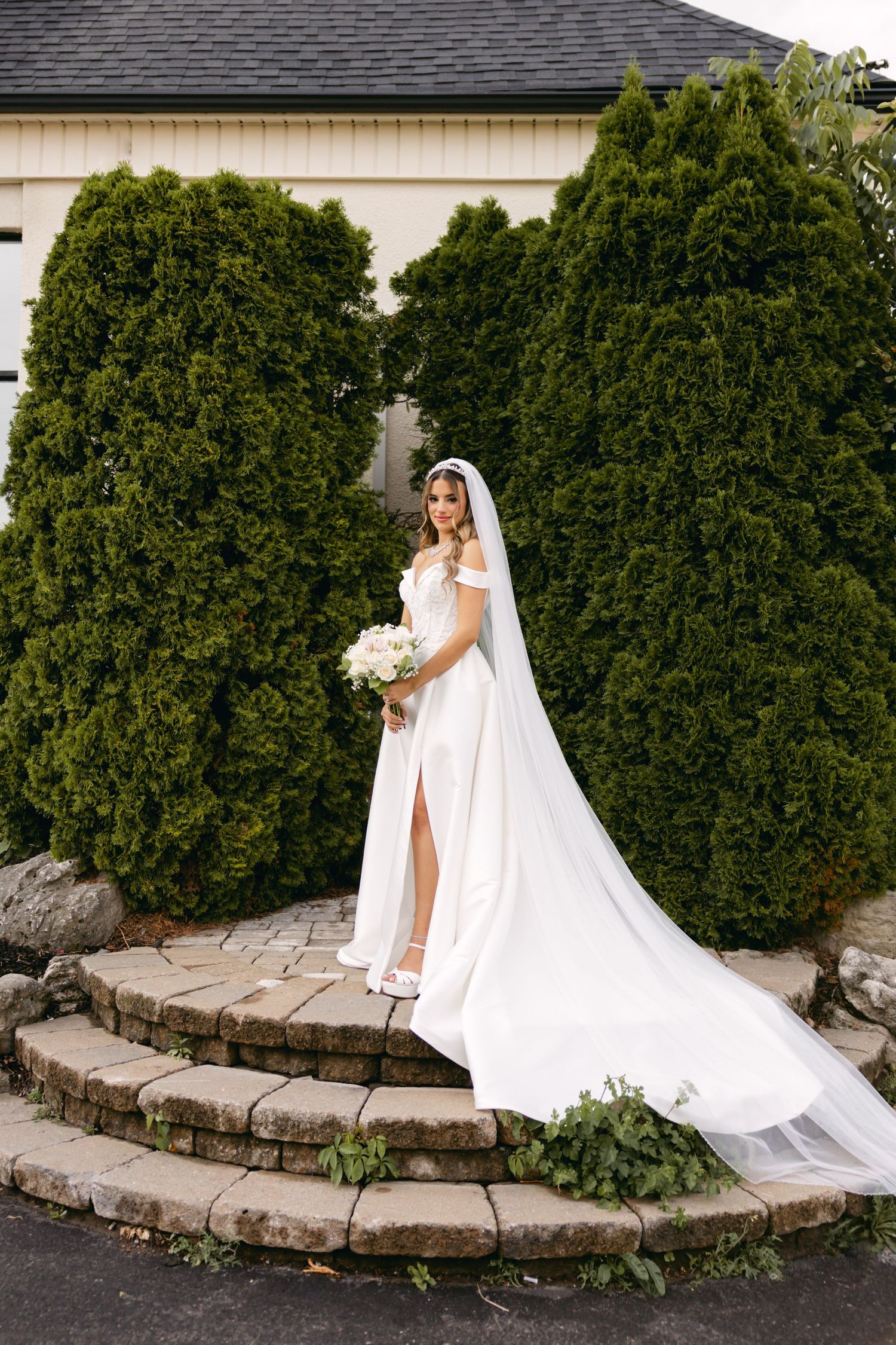 Elegant bridal portrait against landscaped garden wall with flowing cathedral length train.