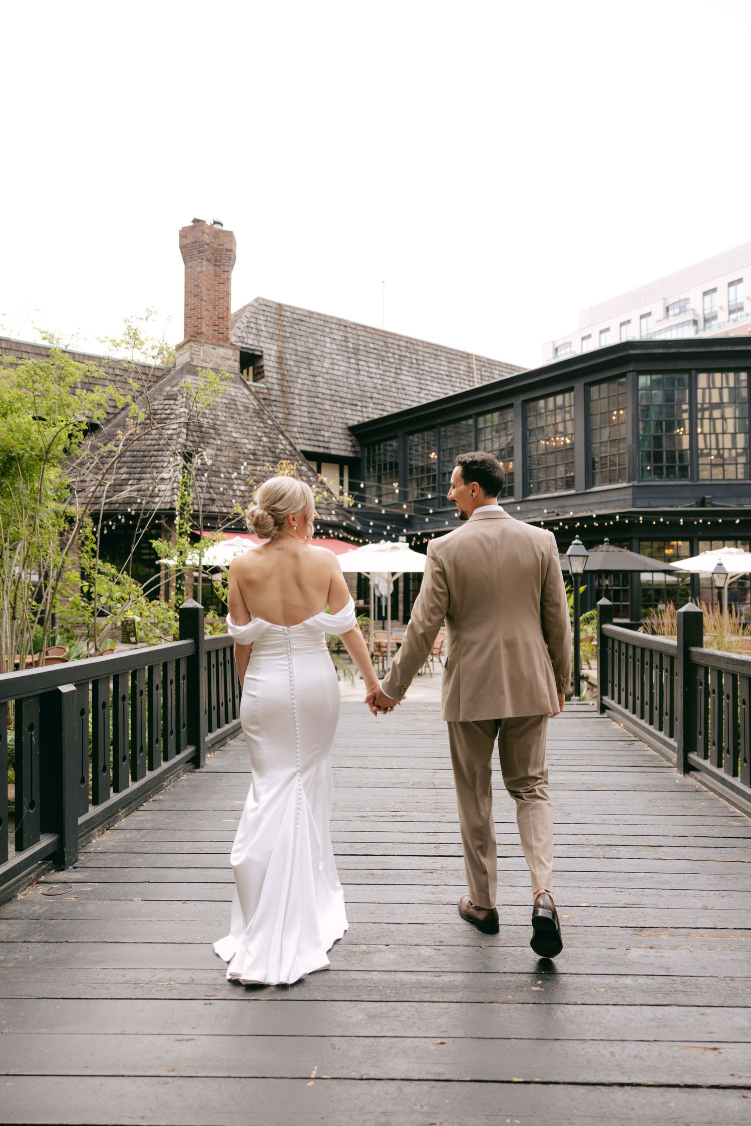 A couple in wedding attire walks hand in hand across a wooden bridge on their special day.