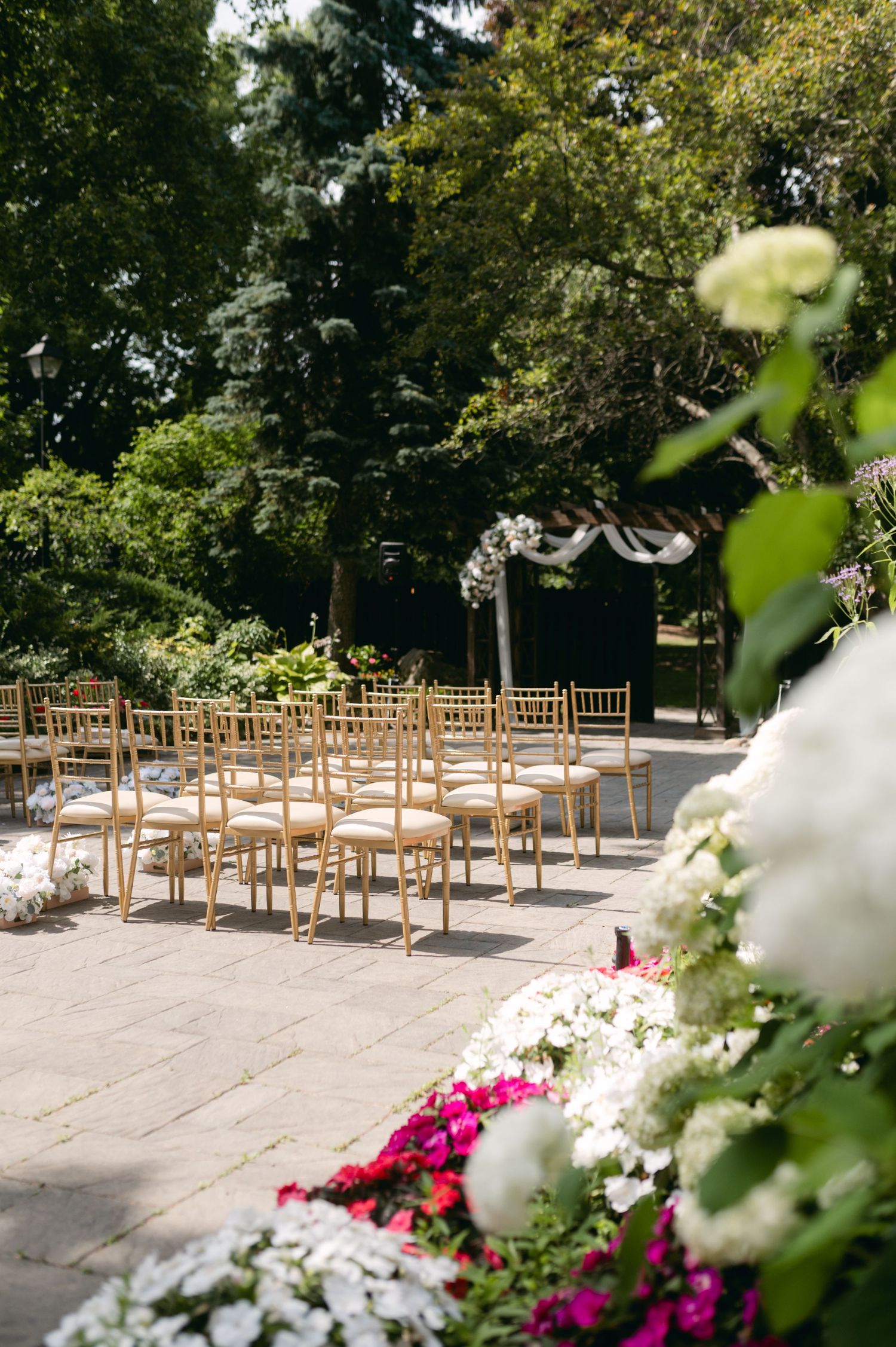 Outdoor wedding ceremony setup with wooden chairs and floral arch in garden setting.