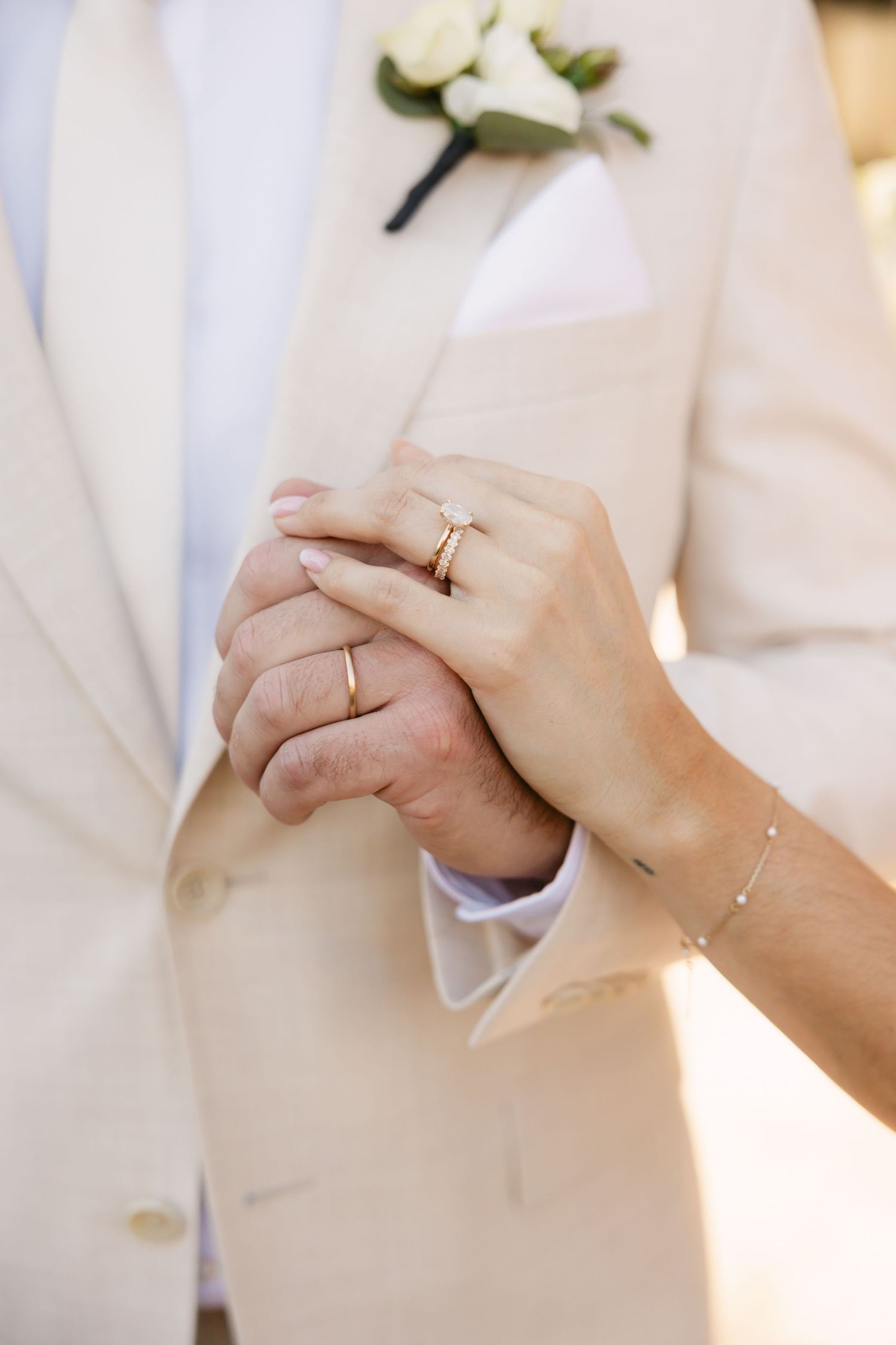Close-up of newlyweds' hands showing wedding rings against white attire.