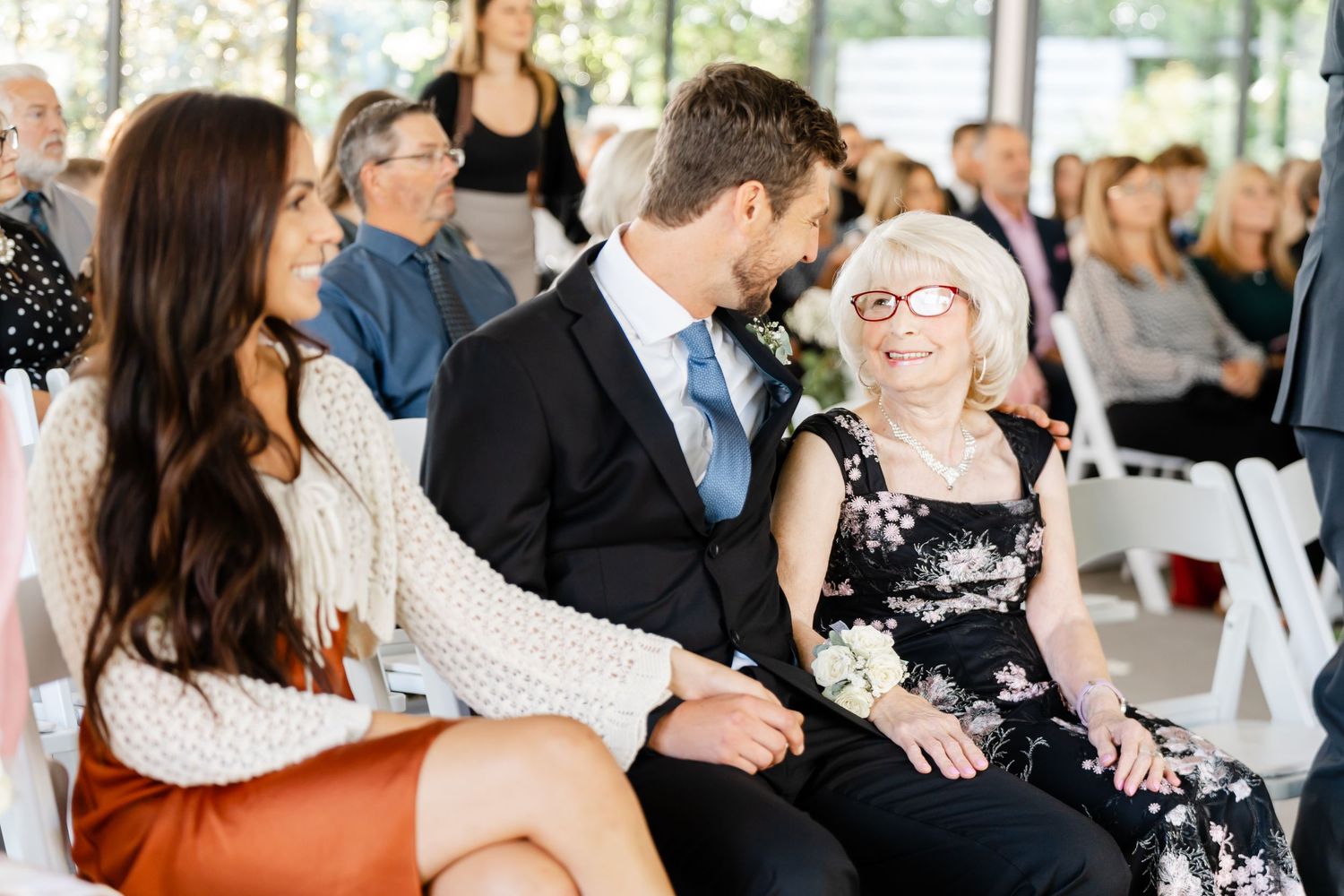 Wedding ceremony attendees seated in white chairs during outdoor celebration.