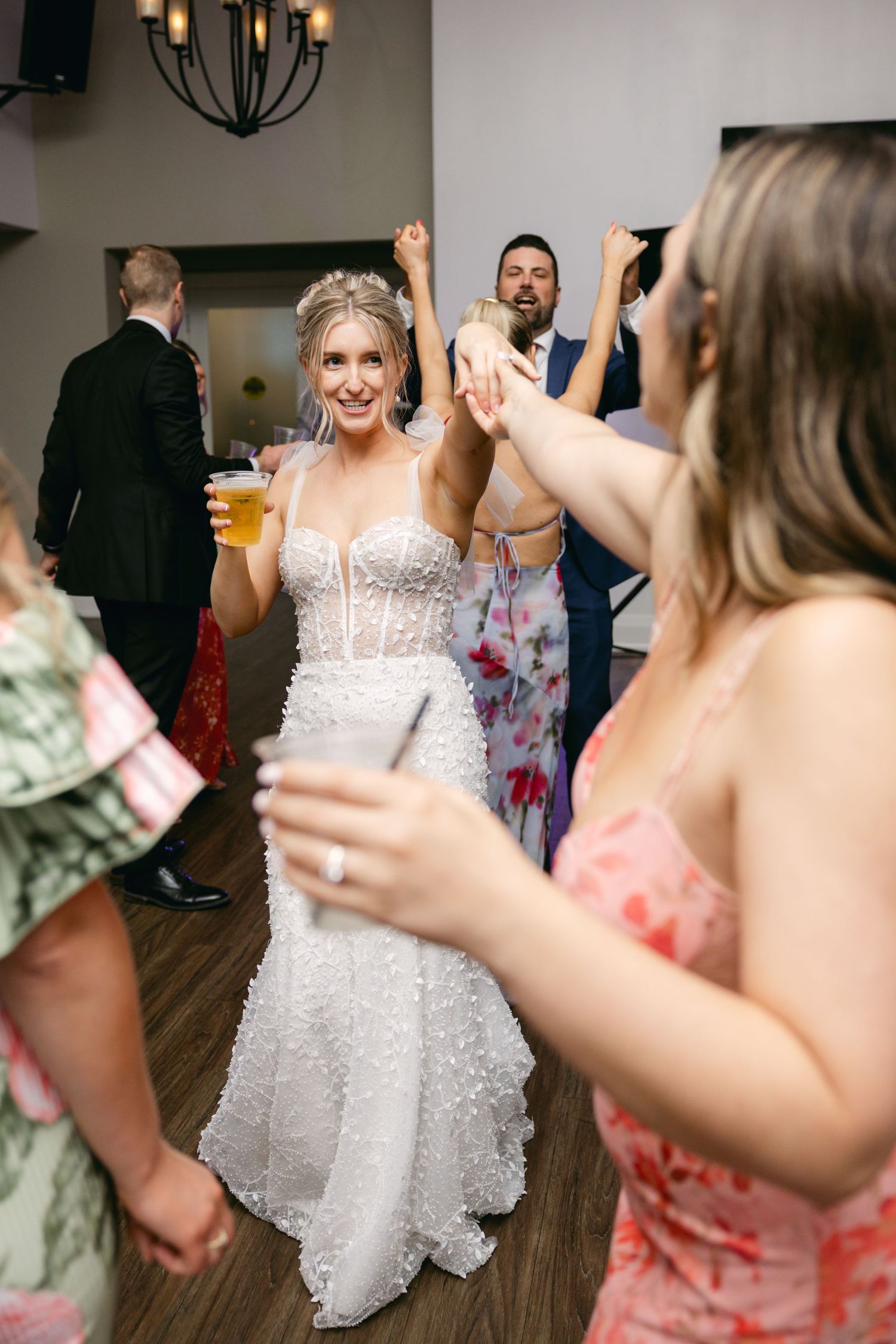 Wedding celebration with guests dancing and twirling in formal attire on wooden dance floor.