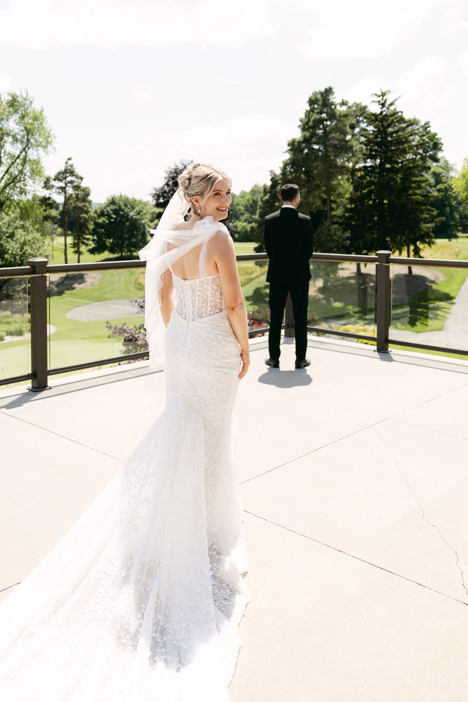 Wedding couple poses on sunny terrace with rolling hills and golf course in background.