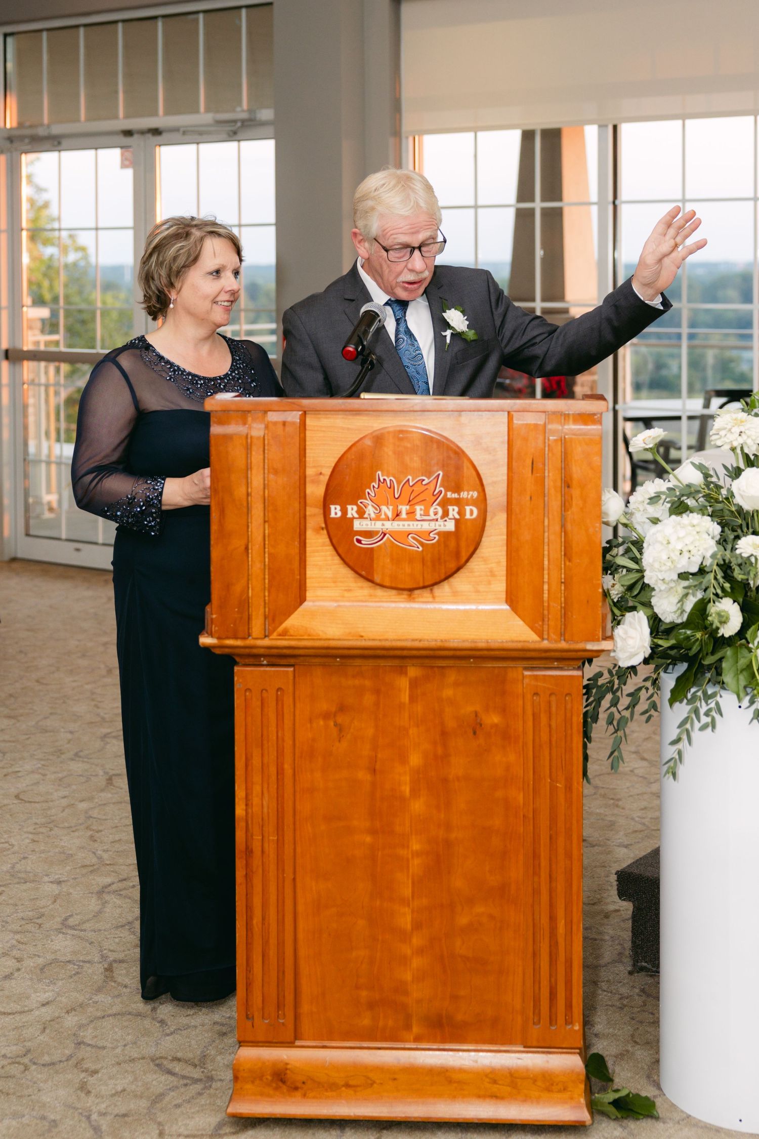 Speakers deliver wedding toasts from a wooden podium with decorative floral arrangements.