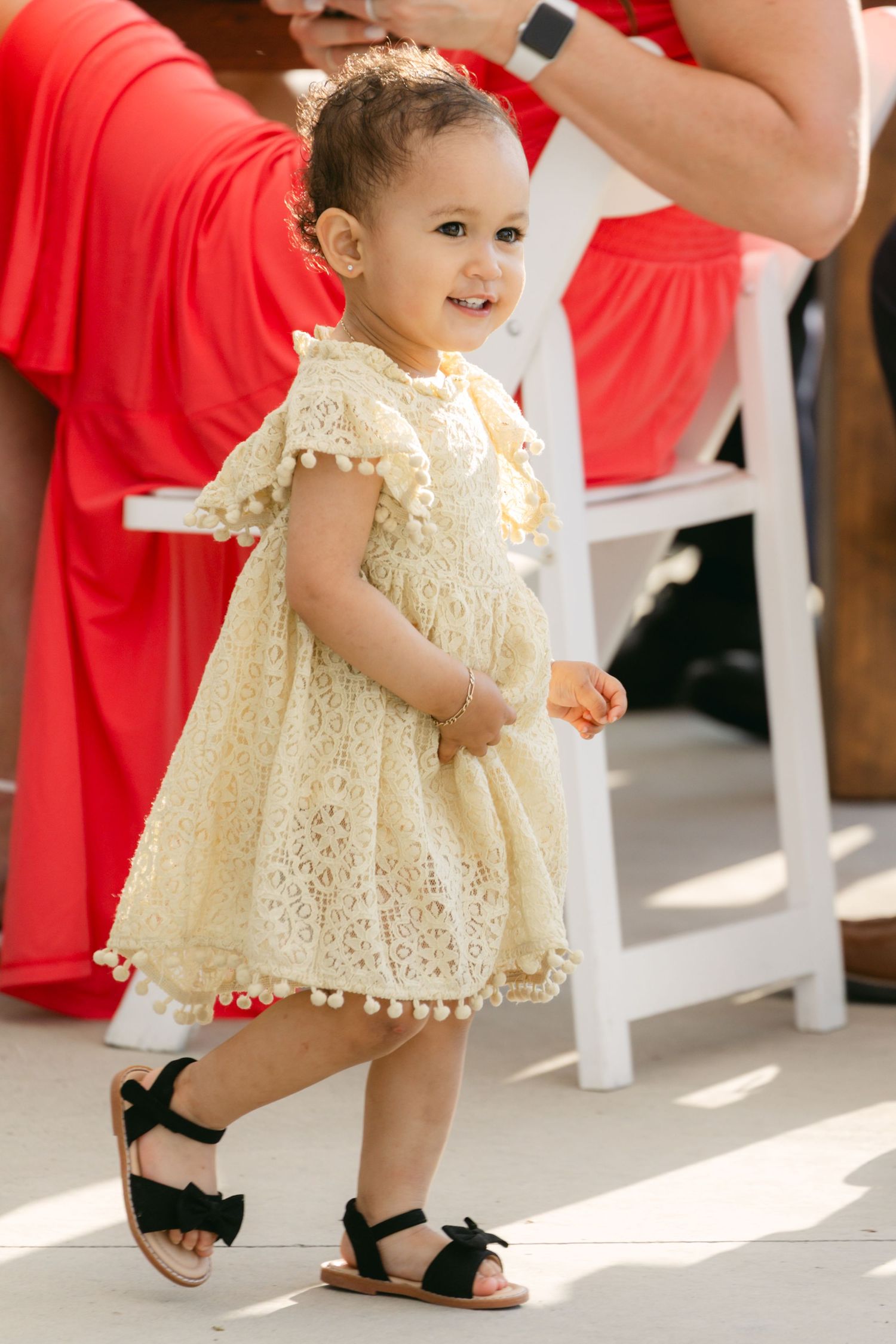 Small child in cream lace dress walks during wedding celebration.