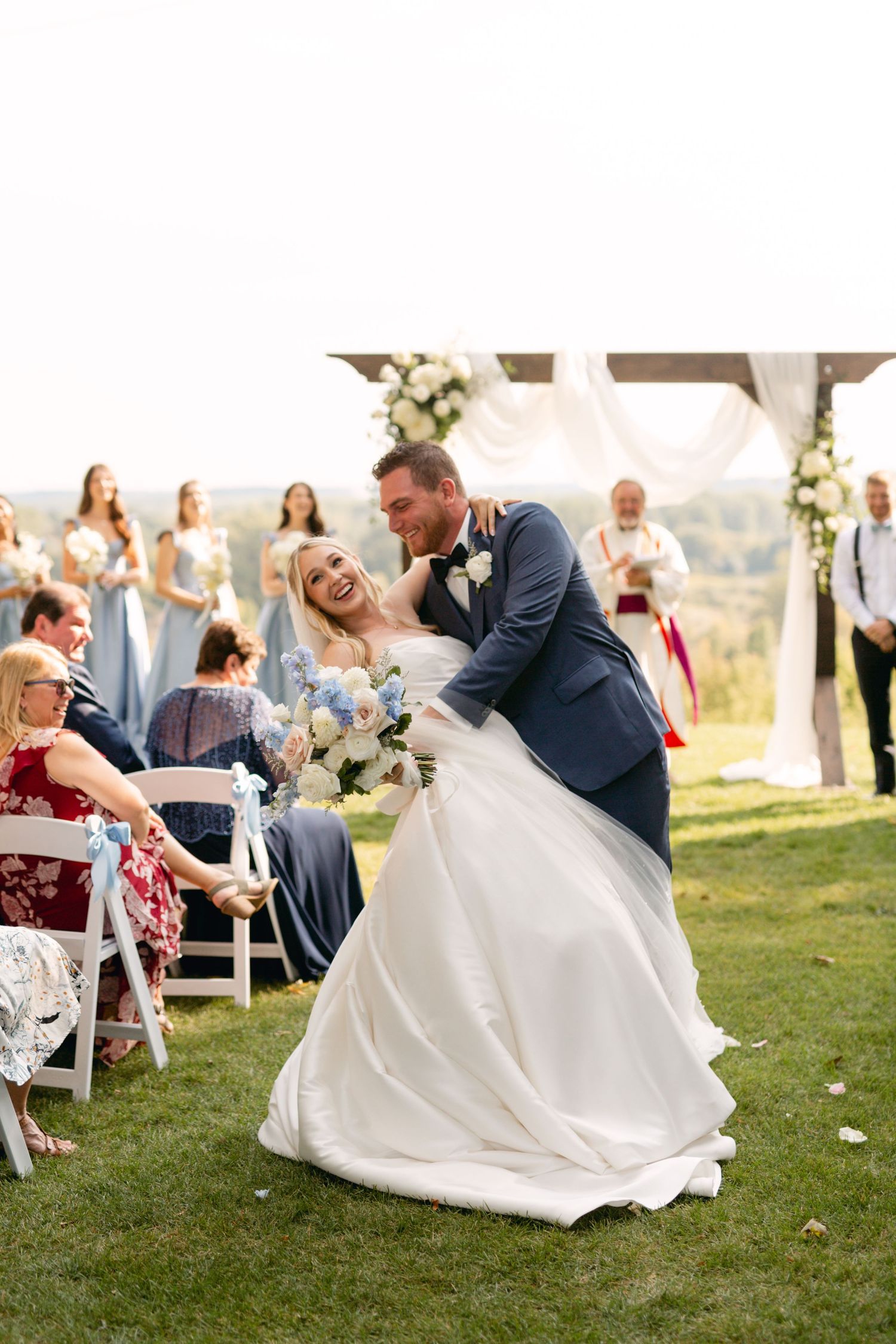 Wedding ceremony moments captured on grassy hillside with white draped altar and chairs.