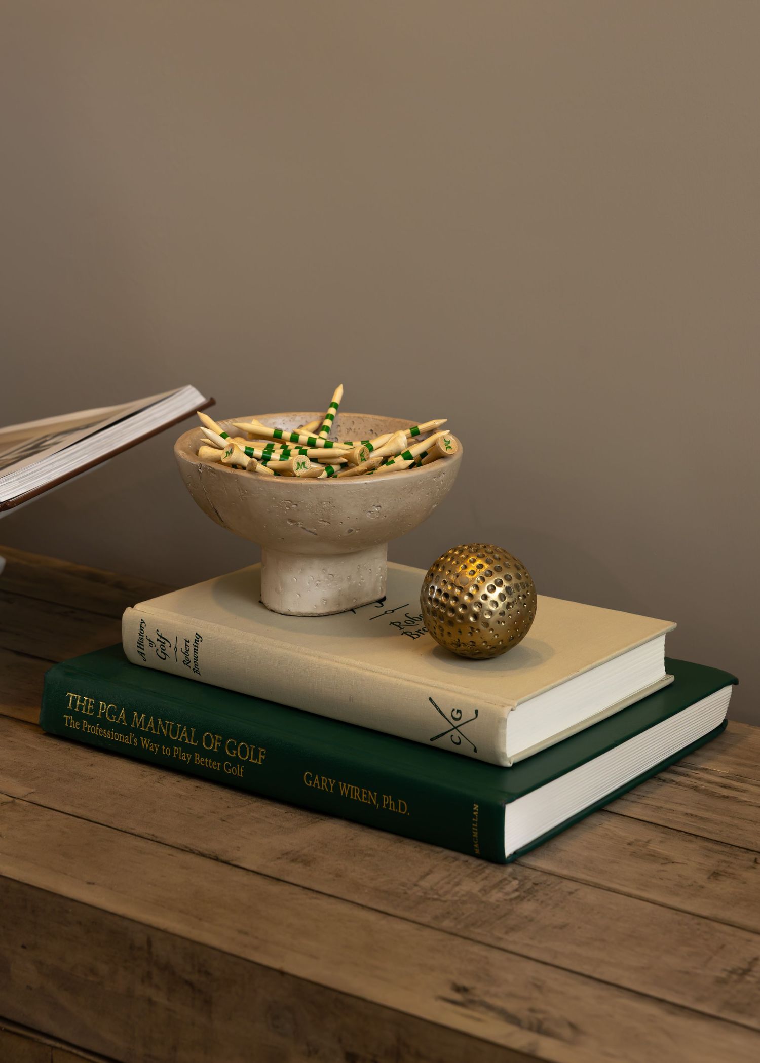 Rustic wooden table styled with green books, decorative bowl, and gold accents.