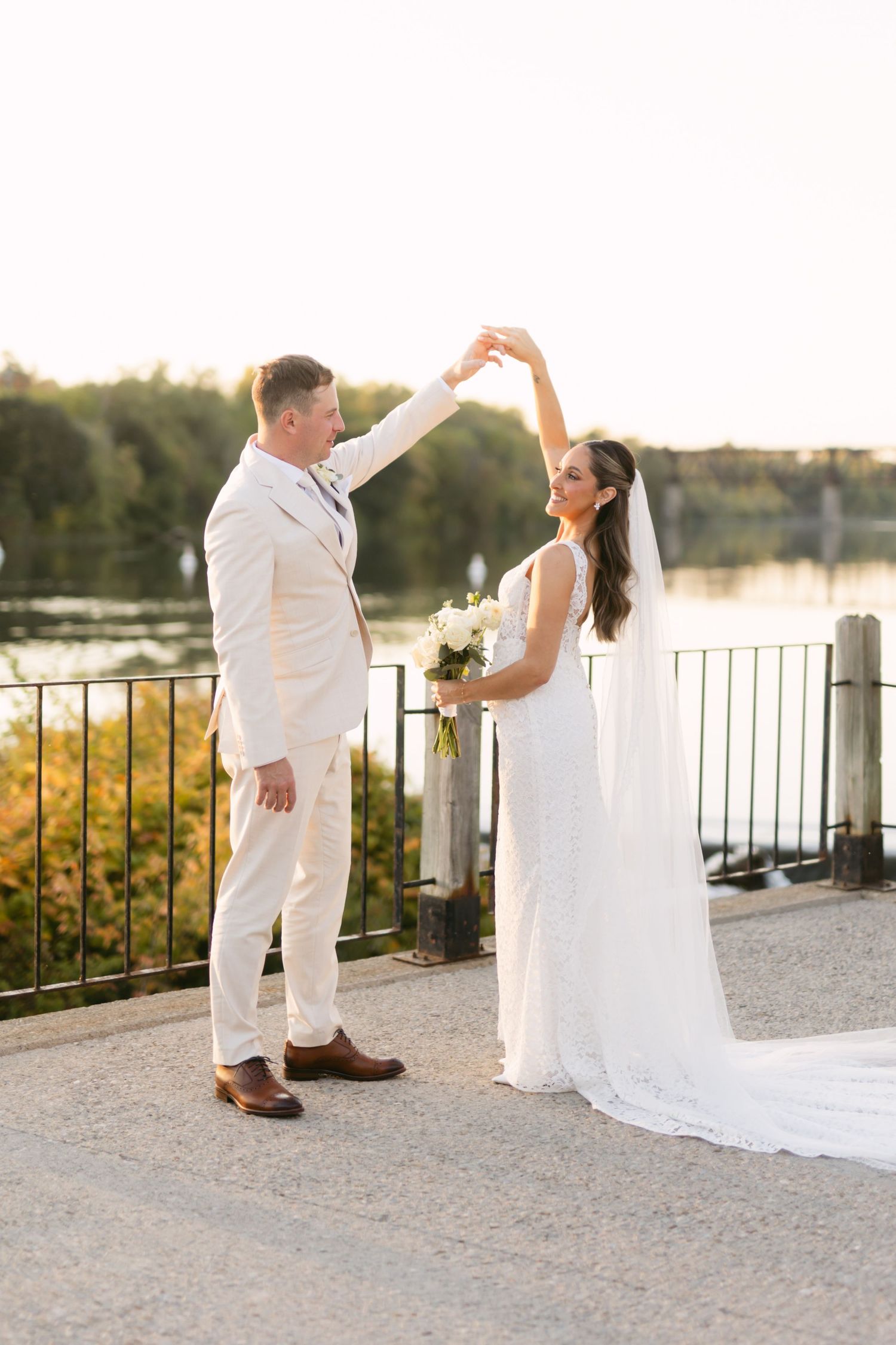 Wedding couple poses on waterfront terrace during golden hour.