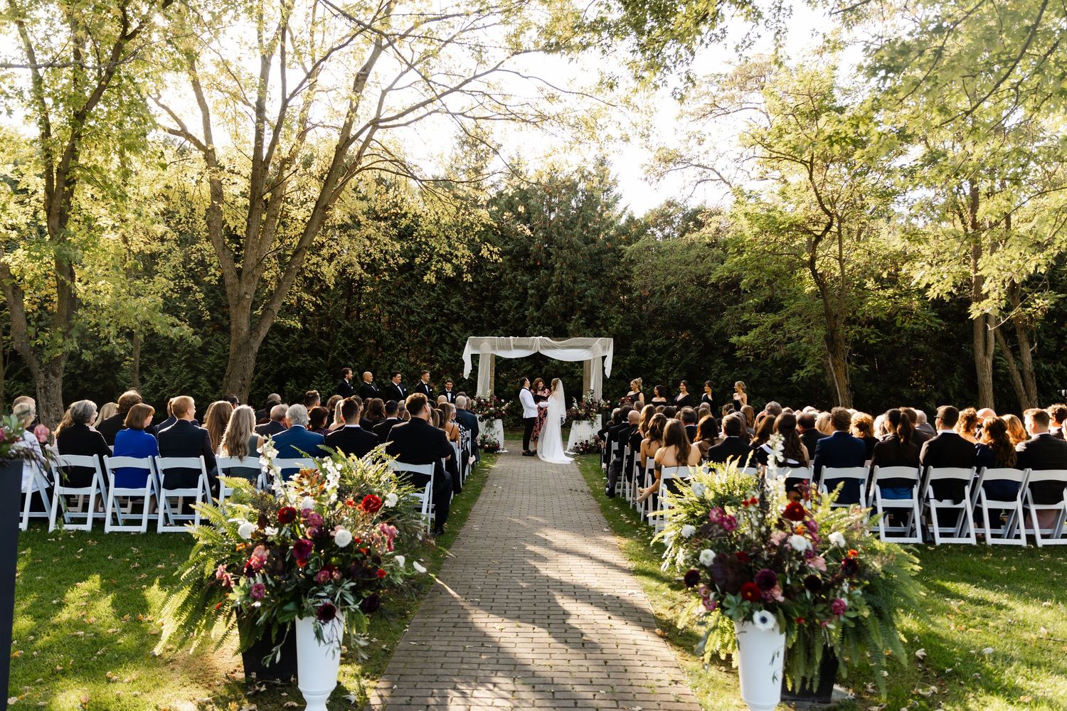 Wide angle view of outdoor wedding ceremony setup with rows of white chairs along stone pathway.