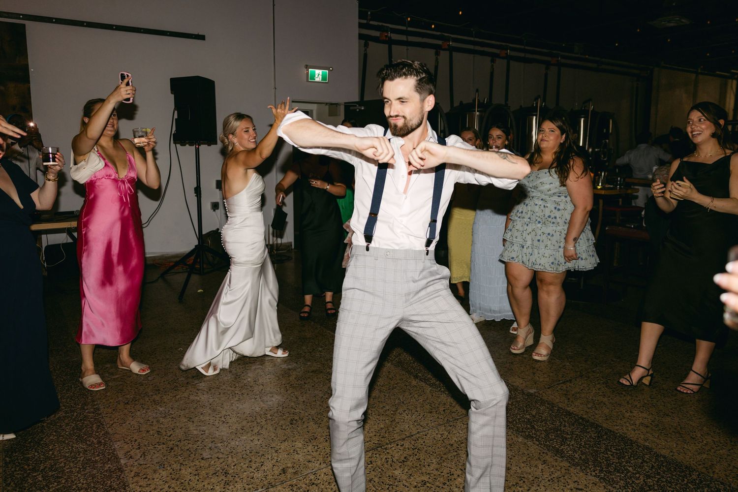 Wedding reception dance floor filled with guests dancing and celebrating in a dimly lit venue.