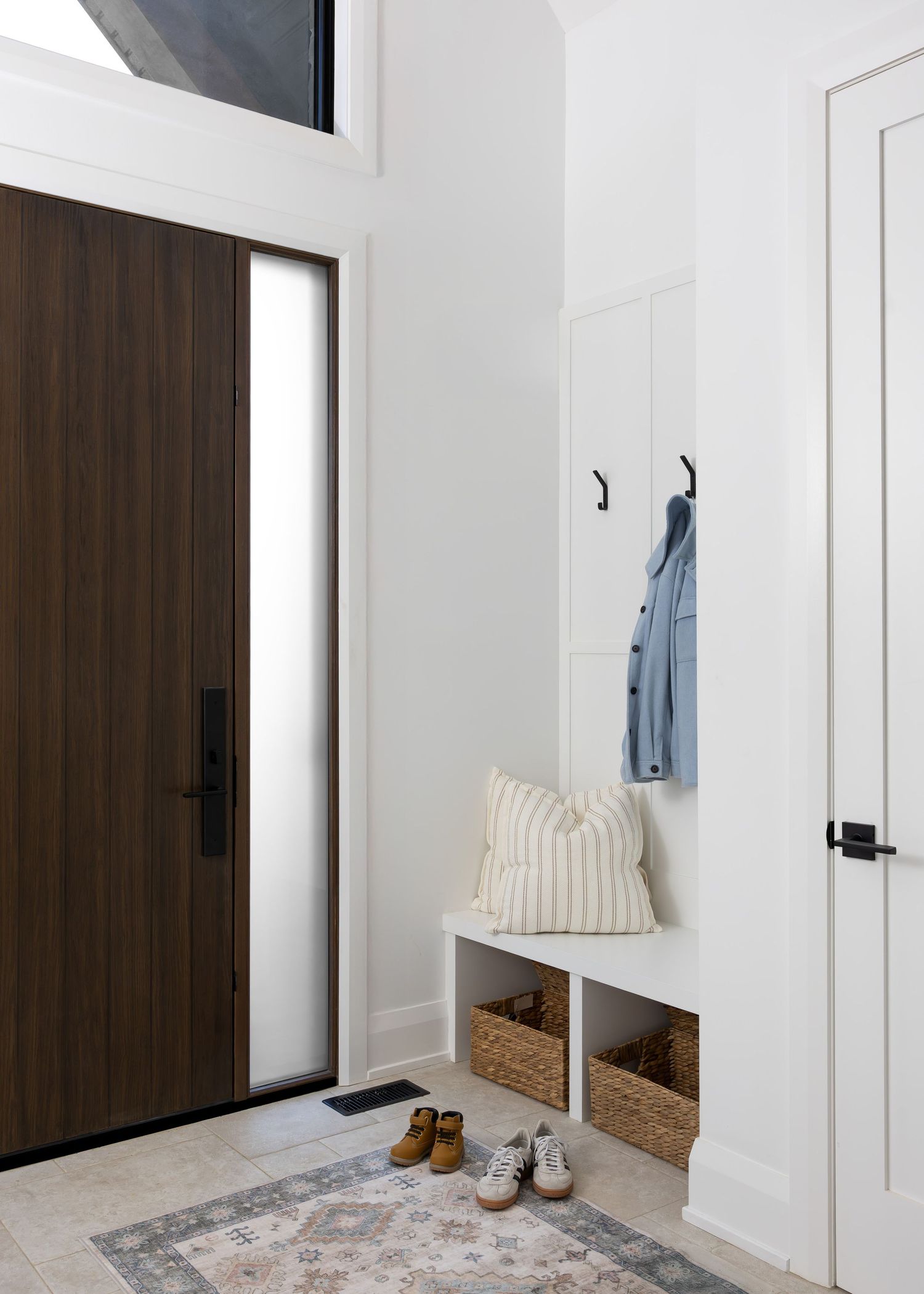 Clean white entryway with dark wood door, built-in storage bench, and modern hooks for coats.