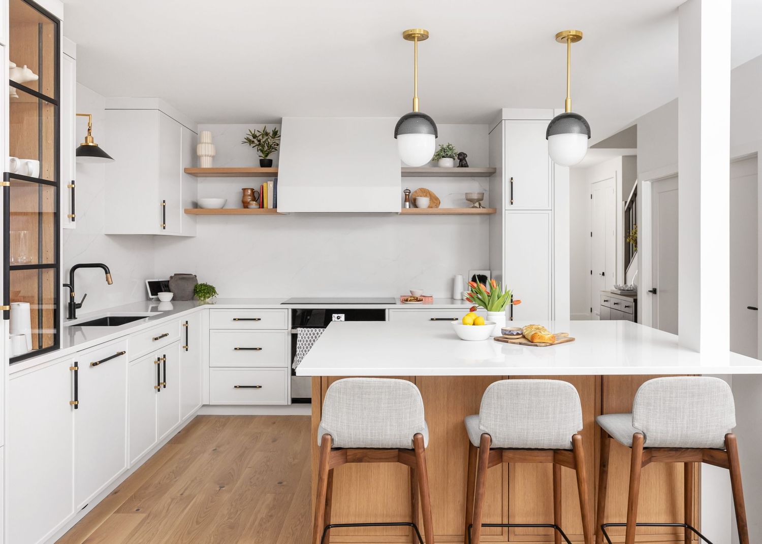 Modern white kitchen with wooden accents, pendant lights, and breakfast bar seating.