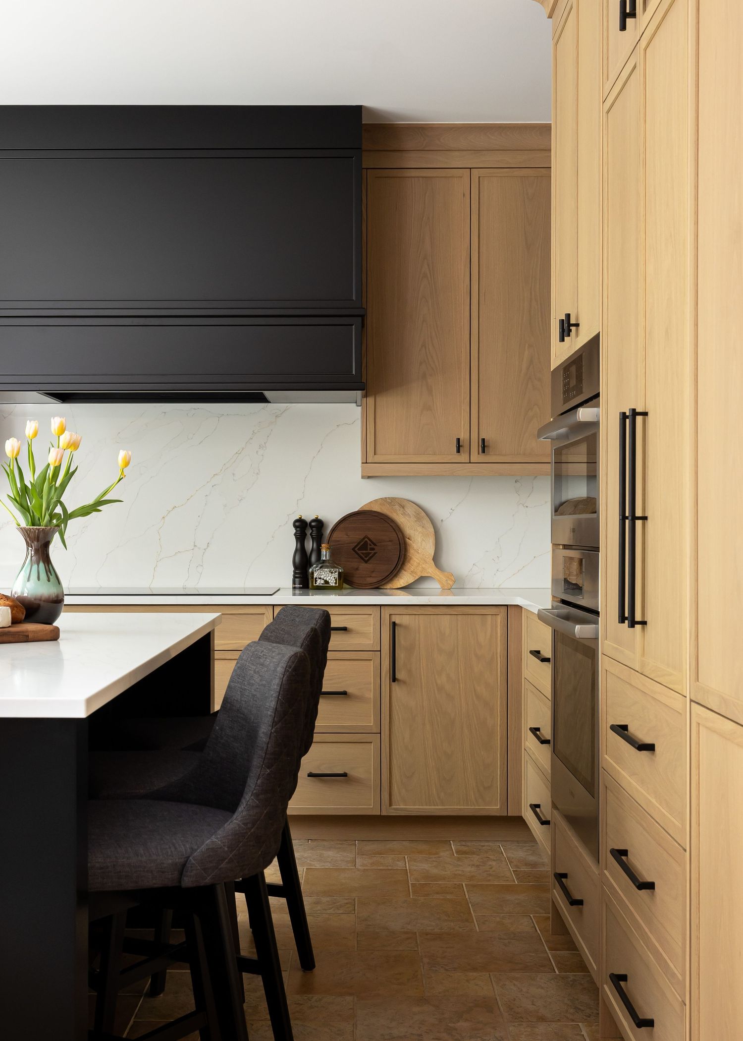 Warm-toned kitchen featuring light wood cabinetry, black accents, and modern appliances.