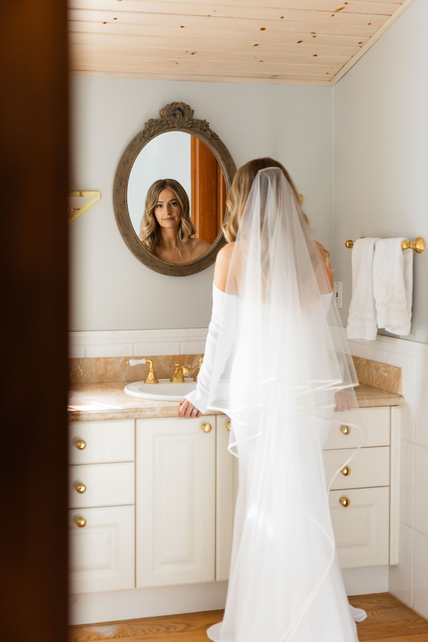 A wedding dress reflection captured in an ornate gold mirror in an elegant bathroom.