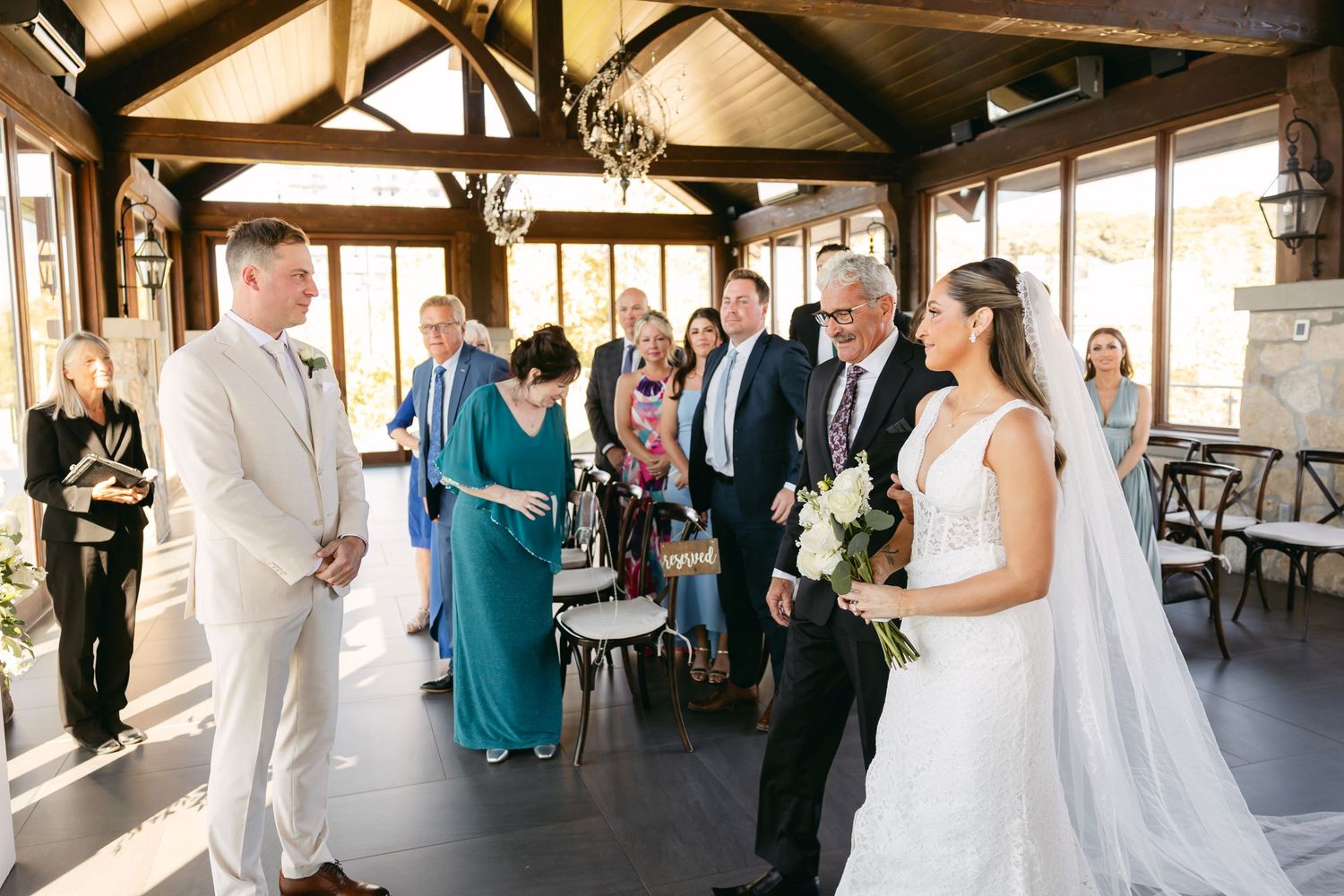 A wedding ceremony takes place in a rustic venue with exposed beams and large windows overlooking a scenic view.