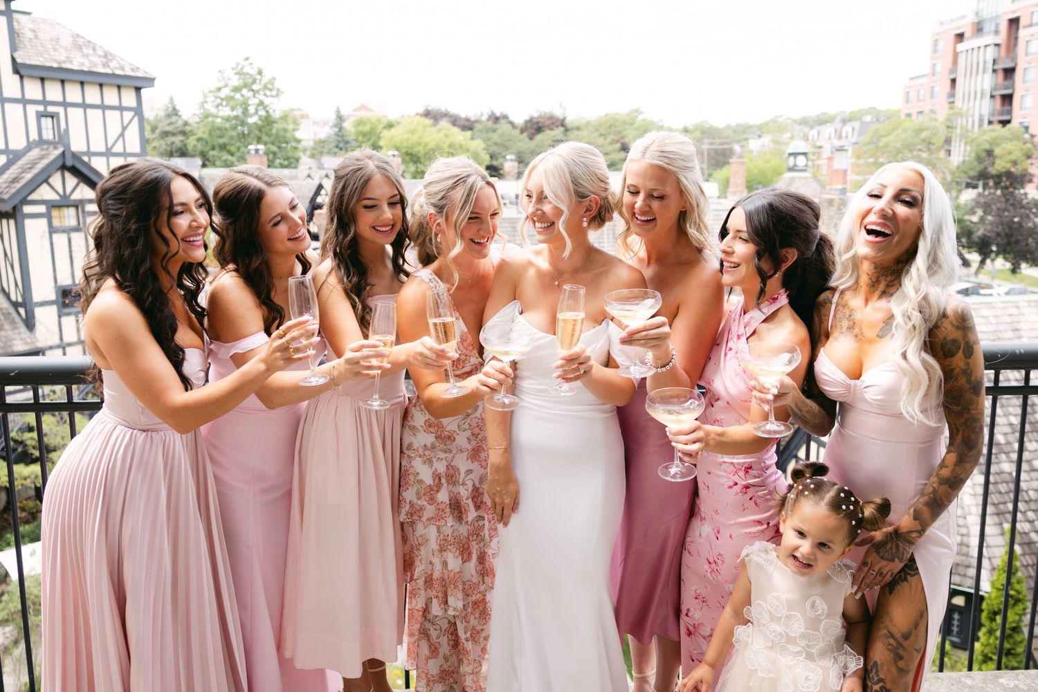 Panoramic shot of bridal party in pink dresses lined up on balcony.